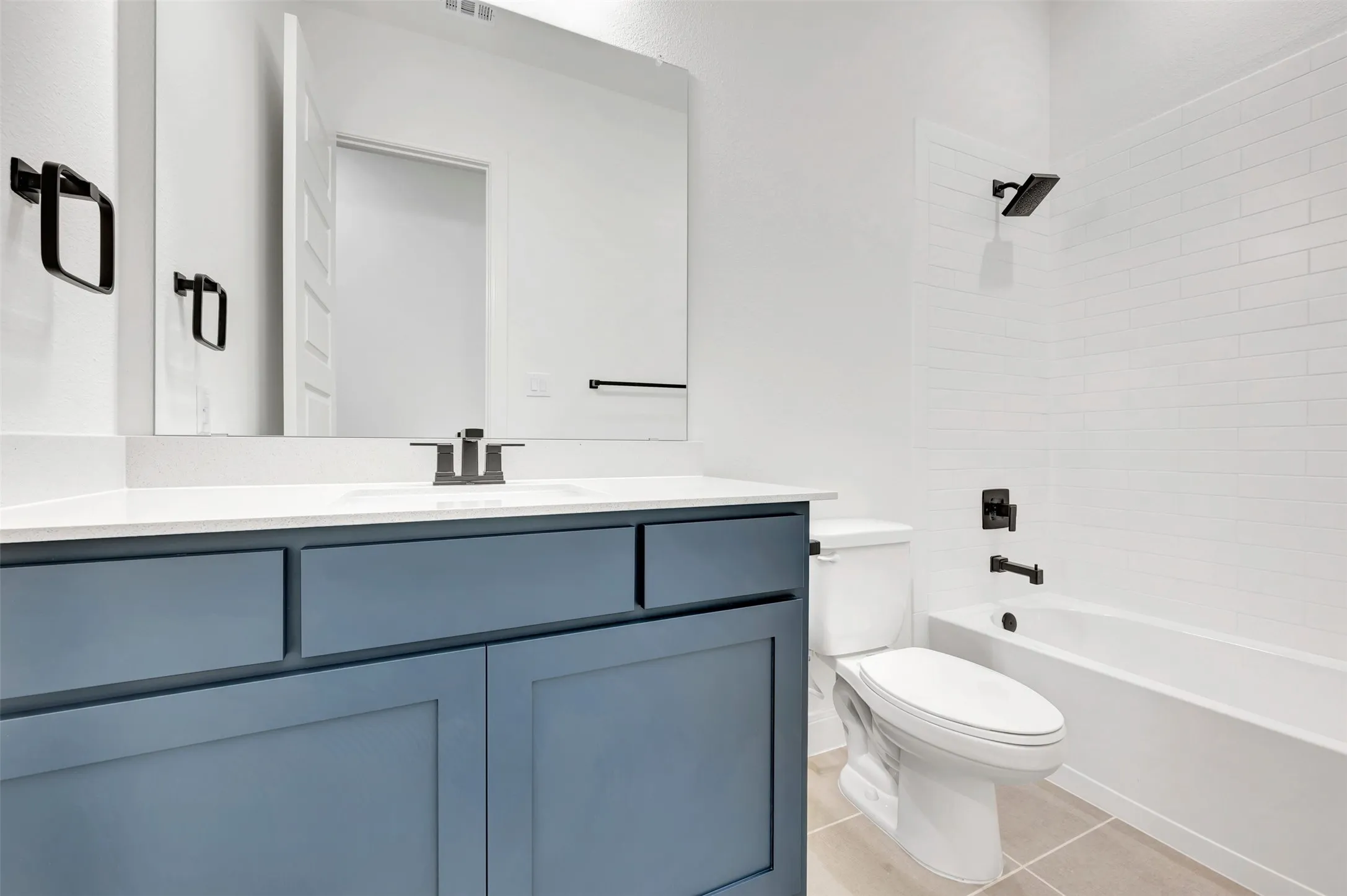 Bathroom featuring a blue vanity with a white countertop, large mirror, and a white subway tile shower surround with black fixtures
