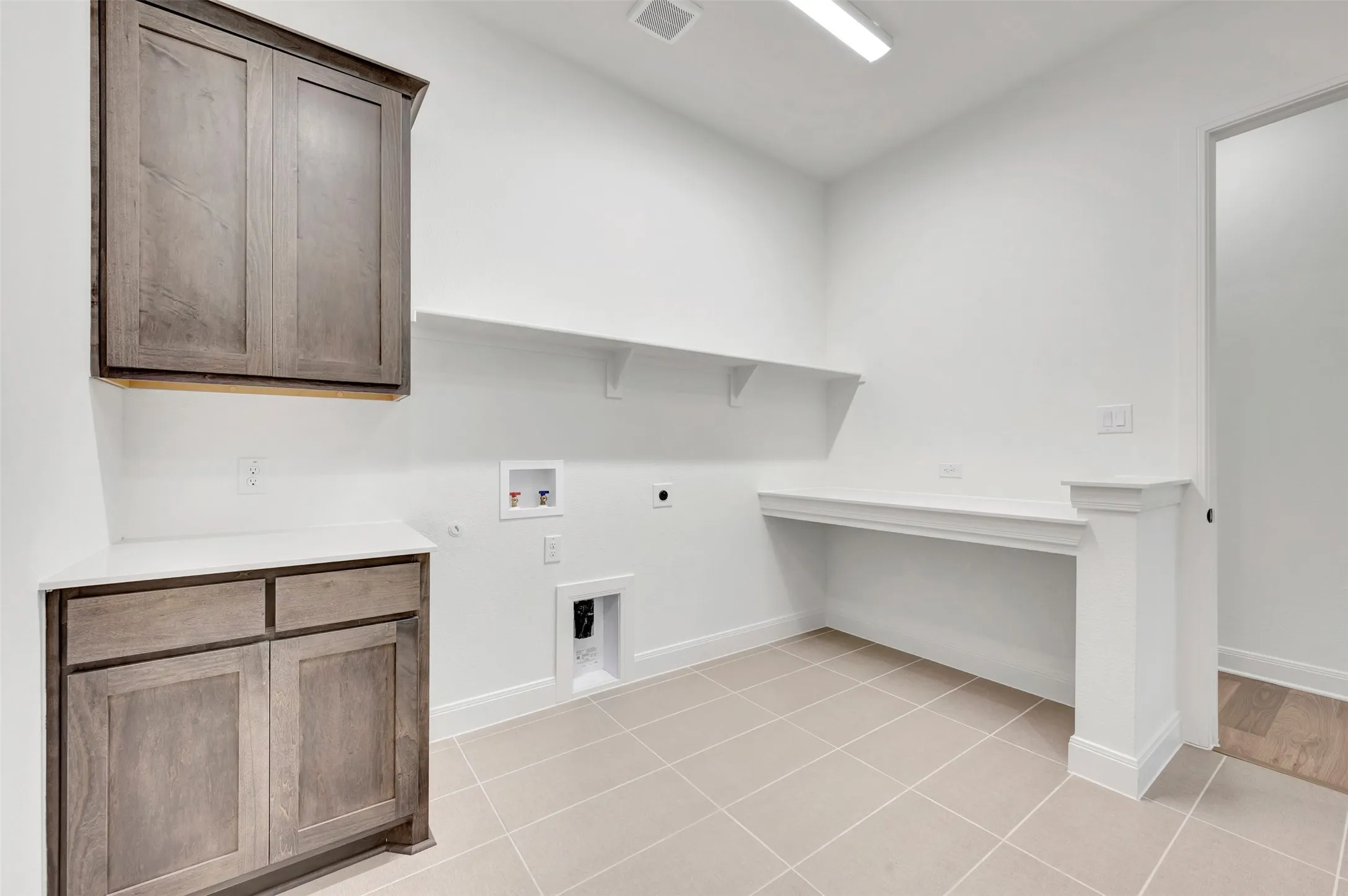 Spacious utility kitchen featuring custom wood-finish cabinetry with dual upper and lower storage units, tile flooring, built-in countertop workspace, and recessed ceiling lighting