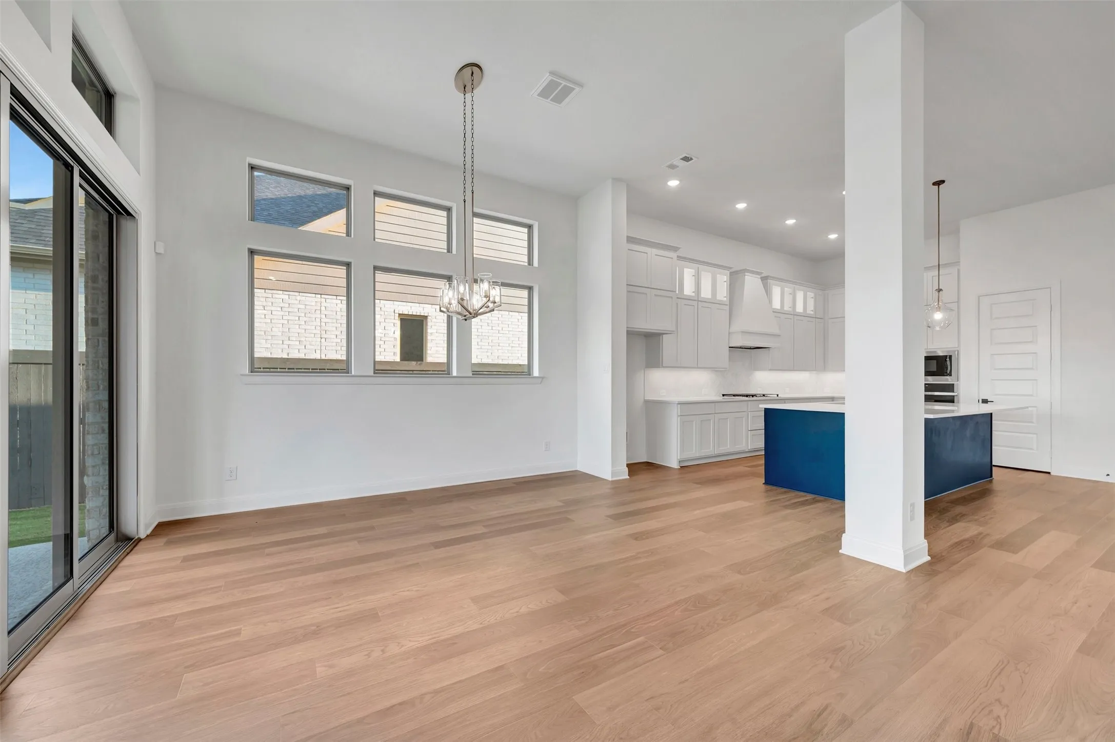 Wood-finish flooring, sliding glass door, contemporary chandelier, white kitchen cabinetry, and a contrasting kitchen island with countertop