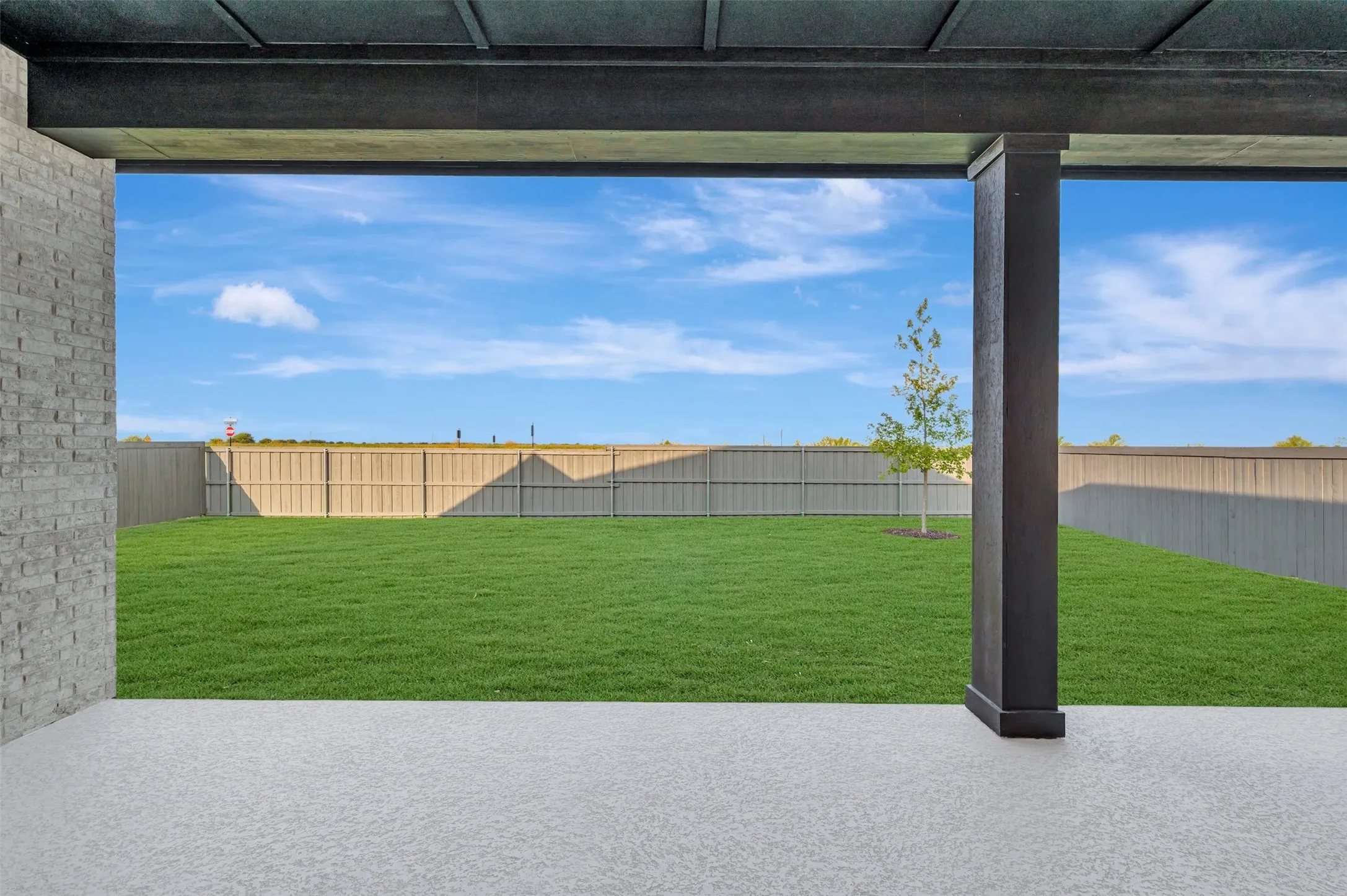 Expansive backyard with mature fenced perimeter and lush lawn, accessed through a covered patio featuring polished concrete flooring and structural steel support columns