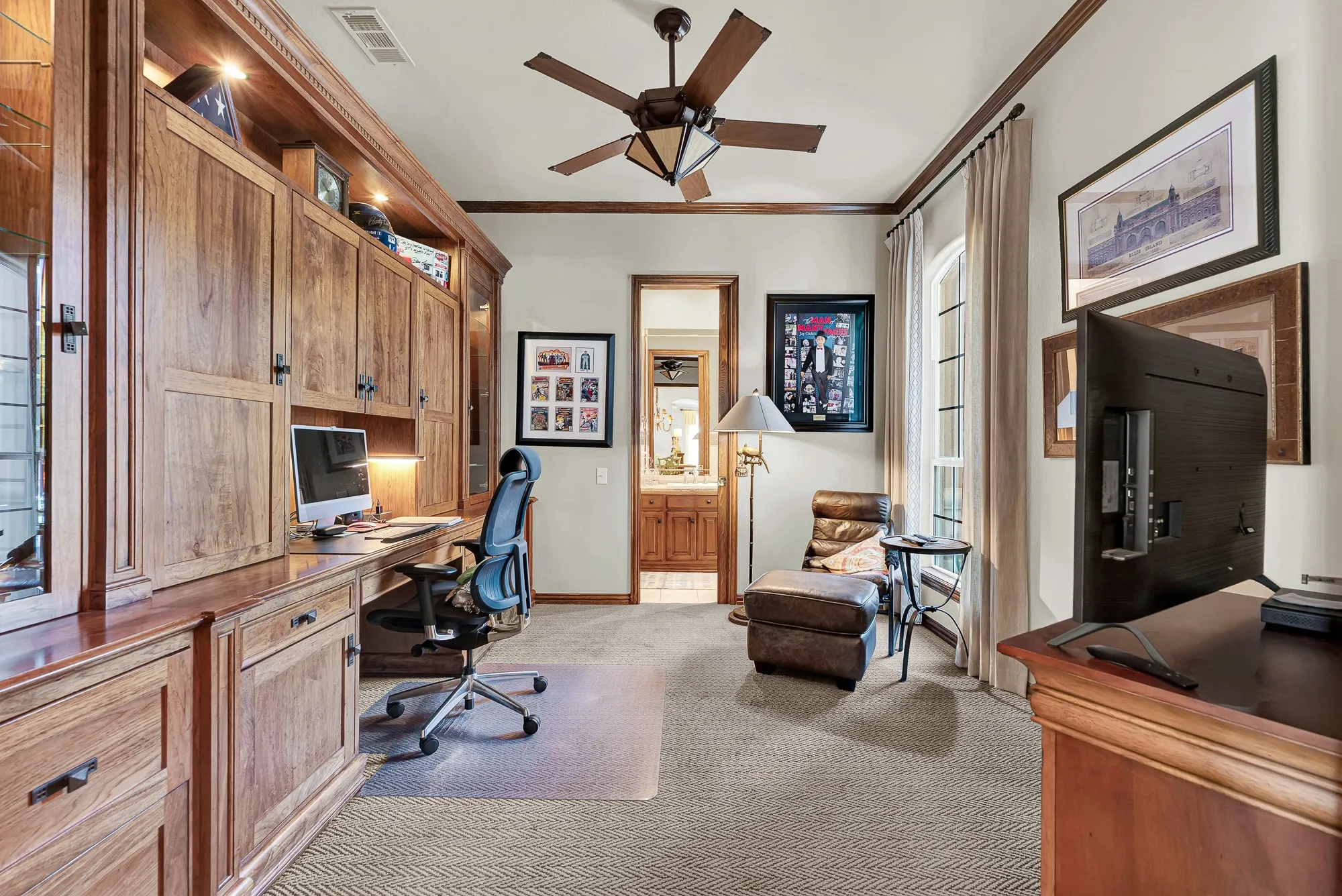 Rich built-in cabinetry, textured carpet, dark wood trim, and an arched window define this versatile first-floor guest suite featuring a private full bath entrance. Whether utilized as a secluded home office or a quiet main-level bedroom for overnight visitors, this flexible space offers ultimate comfort