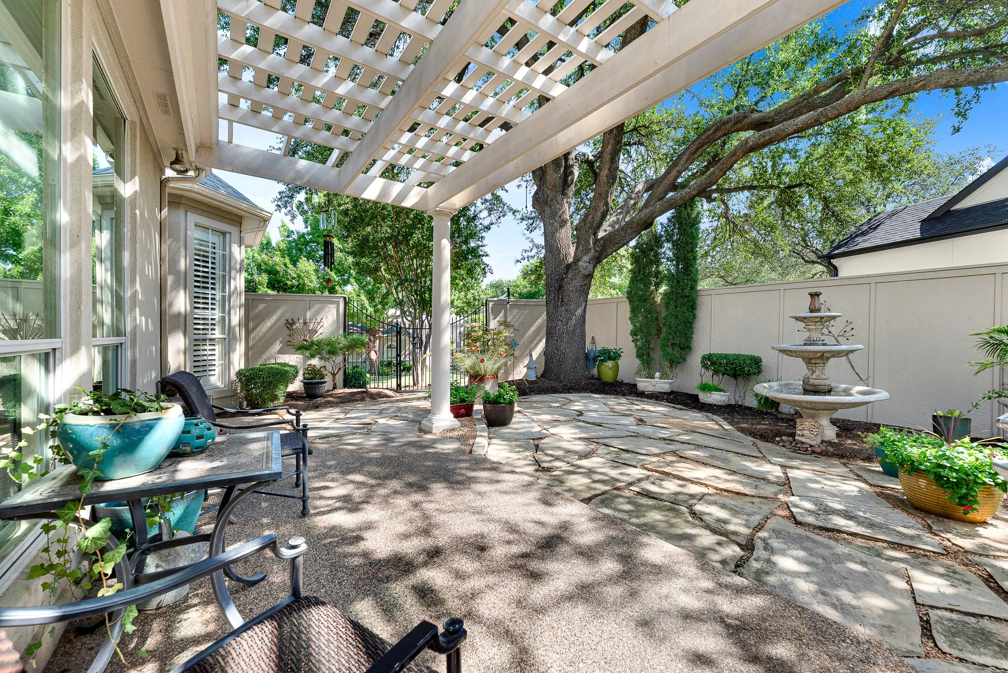 Dappled sunlight filters through towering shade trees over the flagstone courtyard, tiered fountain, and covered patio overhang. You will love entertaining friends in this private, tree-lined oasis that feels worlds away from the daily hustle