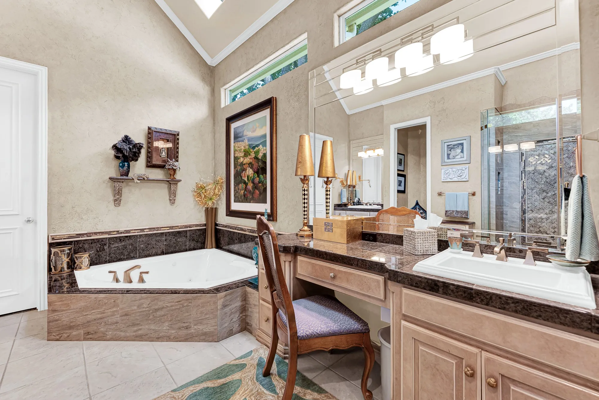 A deep corner jetted tub, rich granite vanity counter, vanity seating area, and overhead transom windows set a tranquil scene. You will love soaking away stress at the end of a long day in your personal spa-like sanctuary.