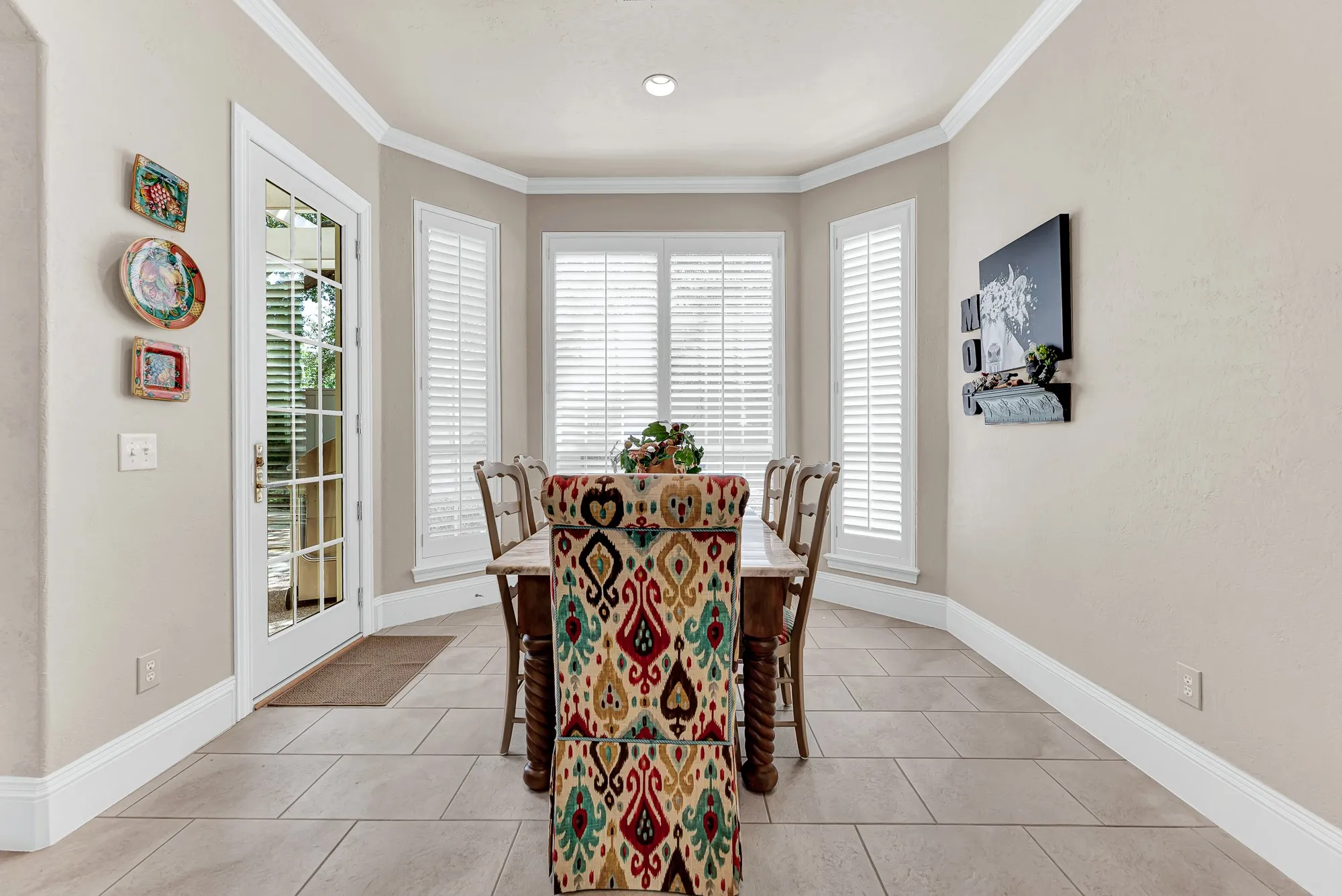 Plantation shutters, crisp crown molding, soft tile flooring, and a glass patio door highlight this bright casual dining alcove. You will love sitting down here for easy morning breakfasts while enjoying warm, natural sunlight filtering through the windows.