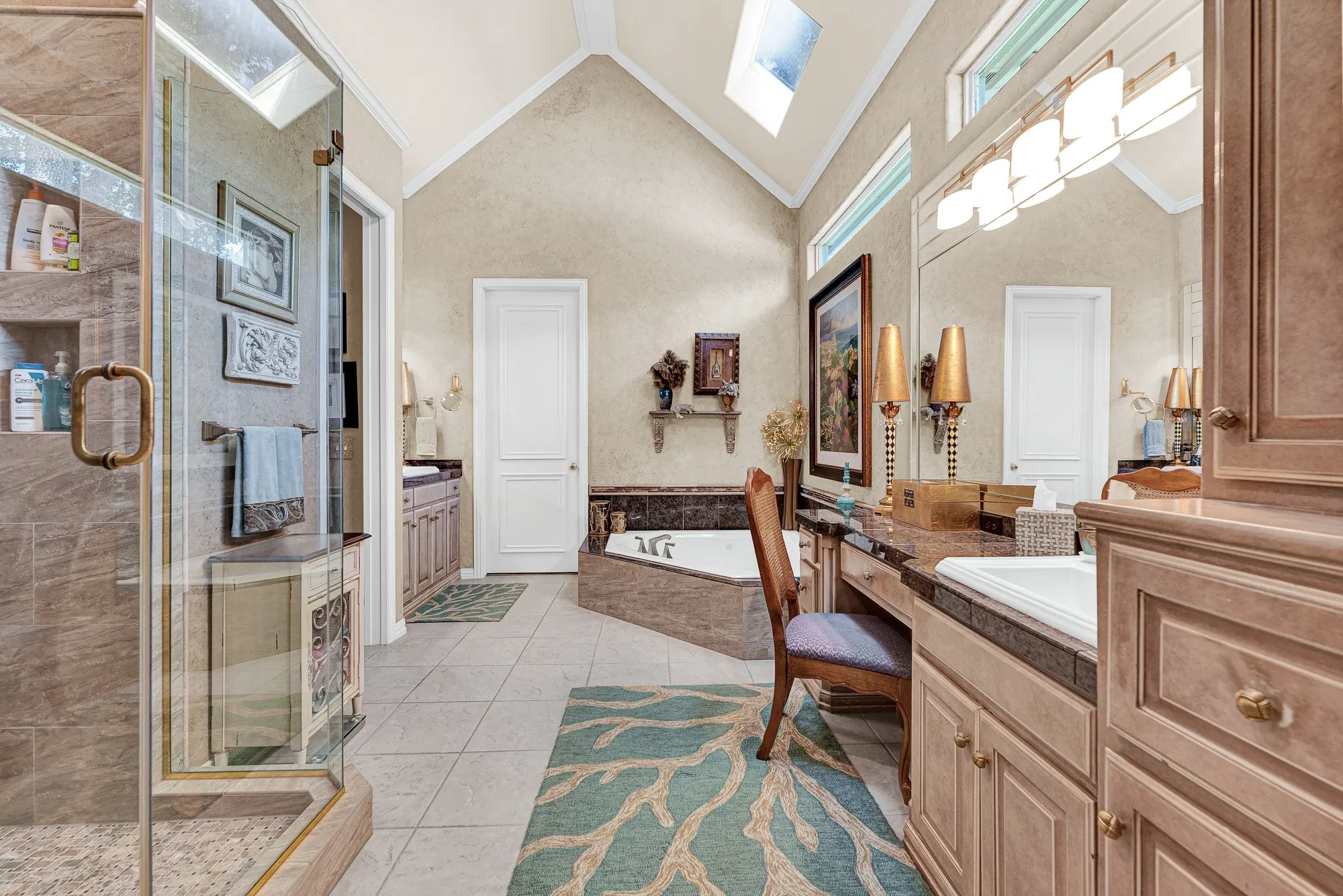 Soaring vaulted ceilings with skylights bring endless natural light into this primary bath featuring a glass shower, soaking tub, and double vanity. Getting ready each morning feels luxurious in this bright, open space.