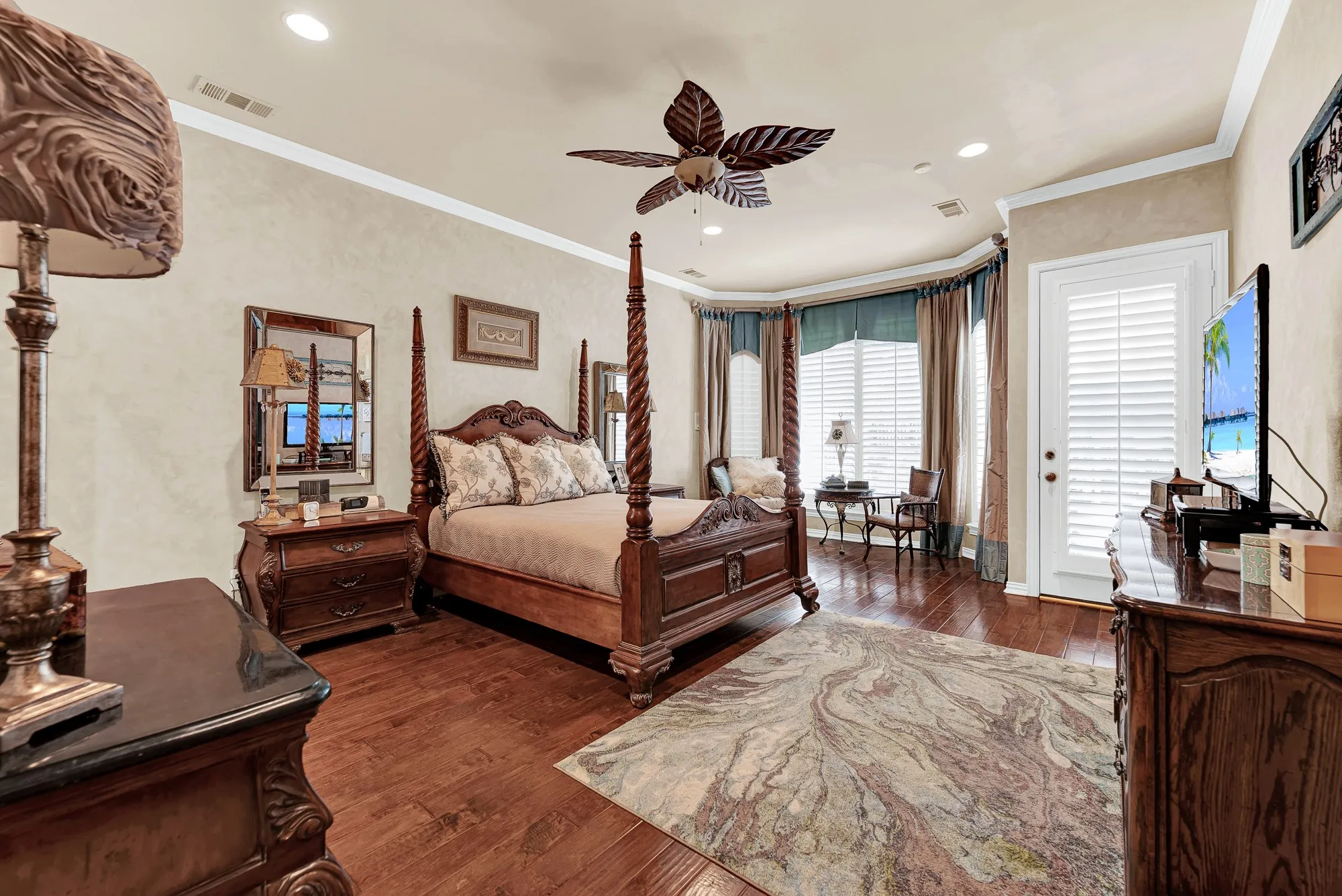 Rich hardwood floors, detailed crown molding, a tropical ceiling fan, and a curved bay window alcove define this spacious primary suite with direct patio access. You will love waking up in this peaceful sanctuary and stepping right outside to enjoy fresh morning air