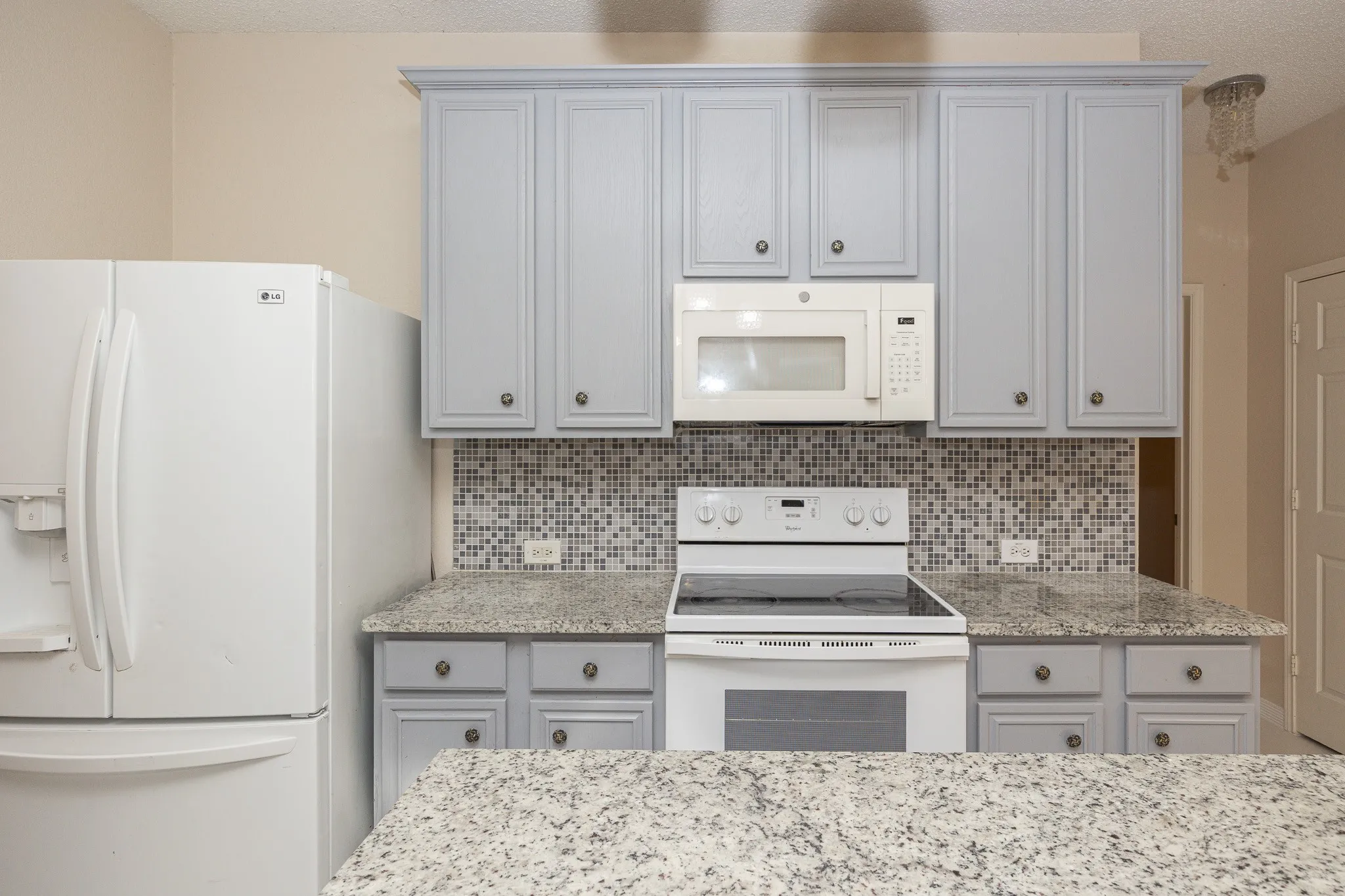 Kitchen featuring light gray cabinetry, speckled countertops, a mosaic tile backsplash, and a built-in microwave
