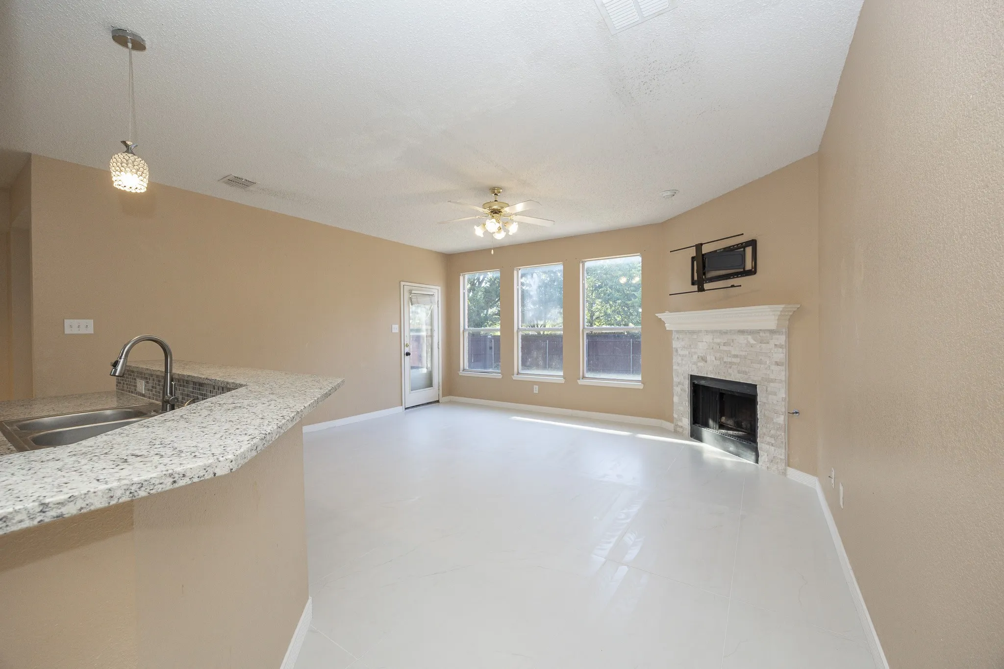 Open-concept living area with light-toned flooring, a stone-clad fireplace, and multiple windows