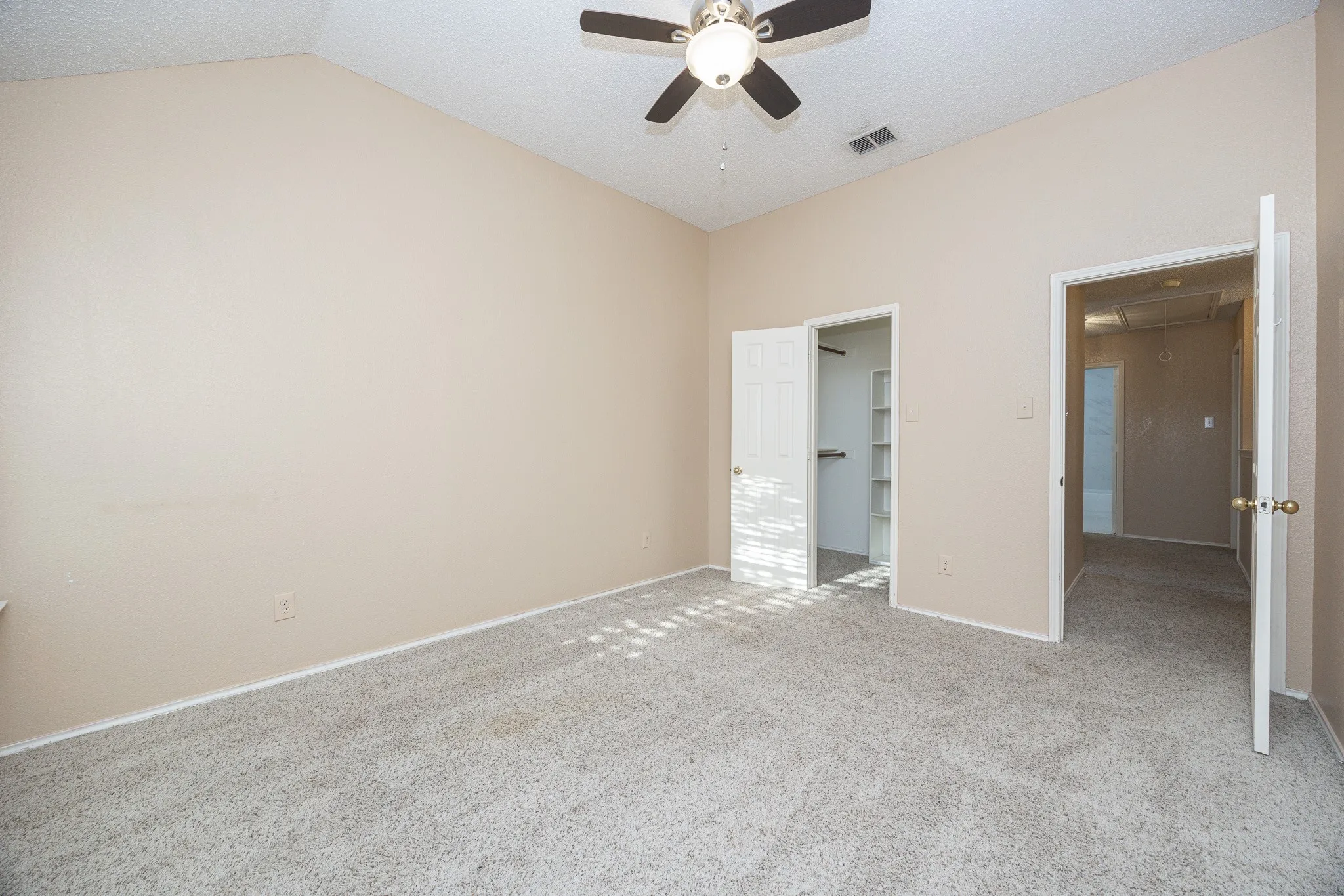 Vaulted ceiling, ceiling fan with integrated lighting, neutral-toned walls, gray-toned carpet, and a built-in closet system