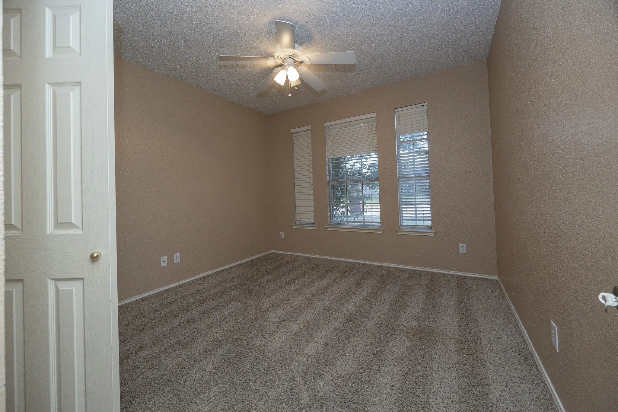 Carpeted room featuring multiple windows with blinds, a ceiling fan with integrated lighting, and neutral wall tones