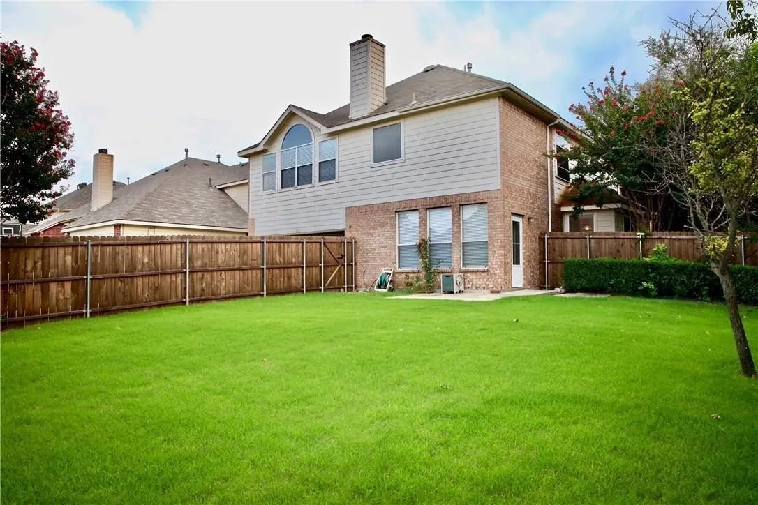 Expansive green lawn, wood privacy fence, brick and siding exterior, arched window, and a patio area