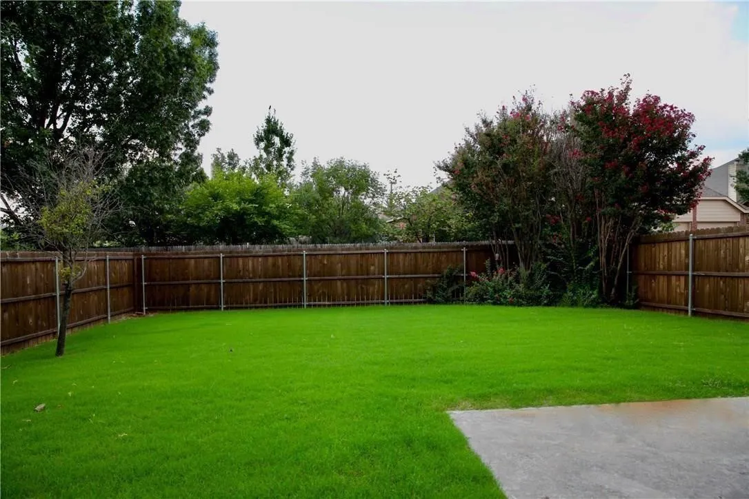 Expansive green lawn with mature perimeter trees, wood privacy fencing, and a concrete patio