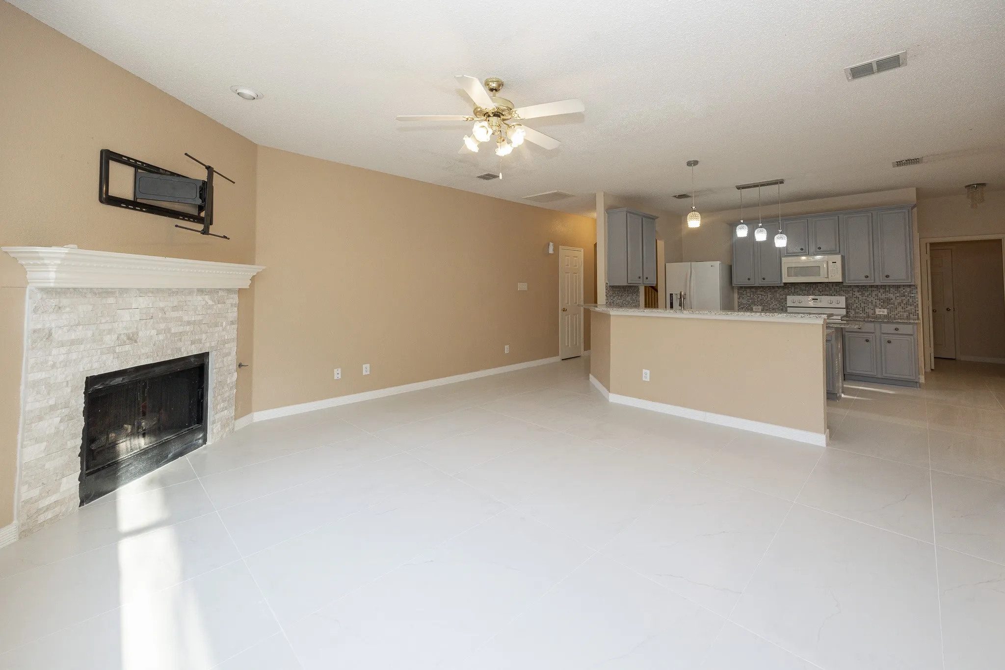 Spacious living area featuring a stone-clad fireplace with a mantel, a ceiling fan, and light tile flooring