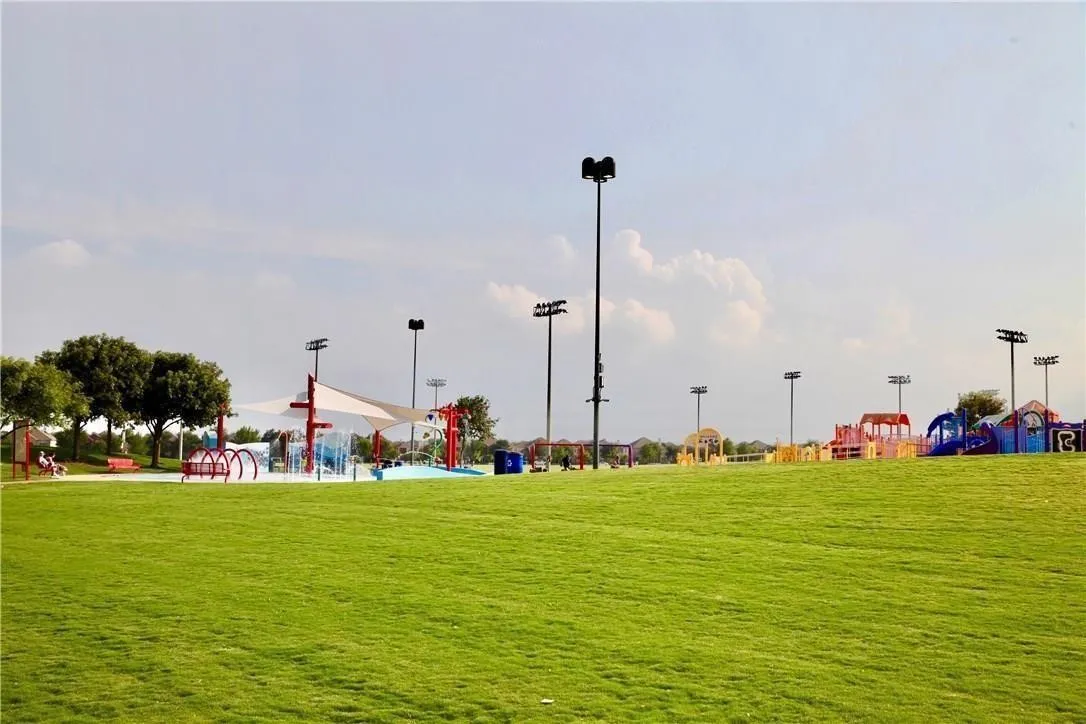 Expansive green space featuring a splash pad with shade structures and a colorful playground area