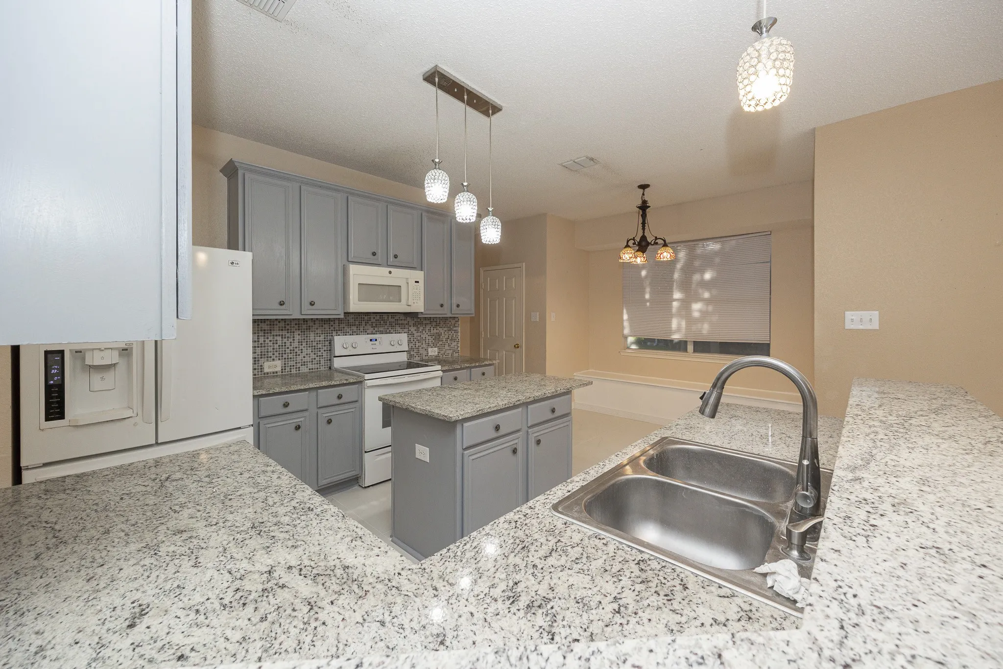 Spacious kitchen featuring light gray cabinetry, granite countertops, stainless steel double basin sink, and a multi-light pendant fixture