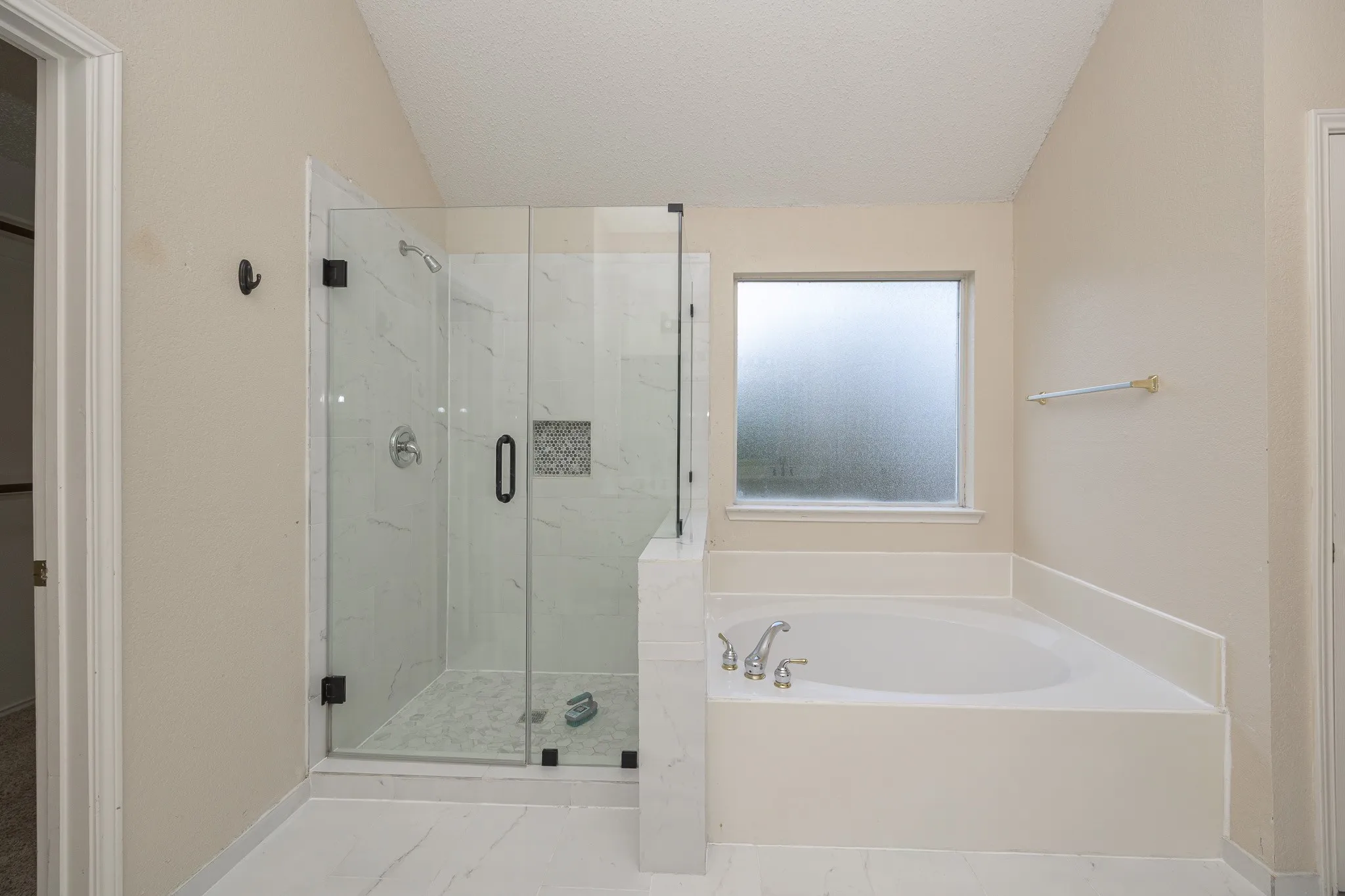Walk-in shower with clear glass enclosure, built-in shelf, and contrasting tile floor