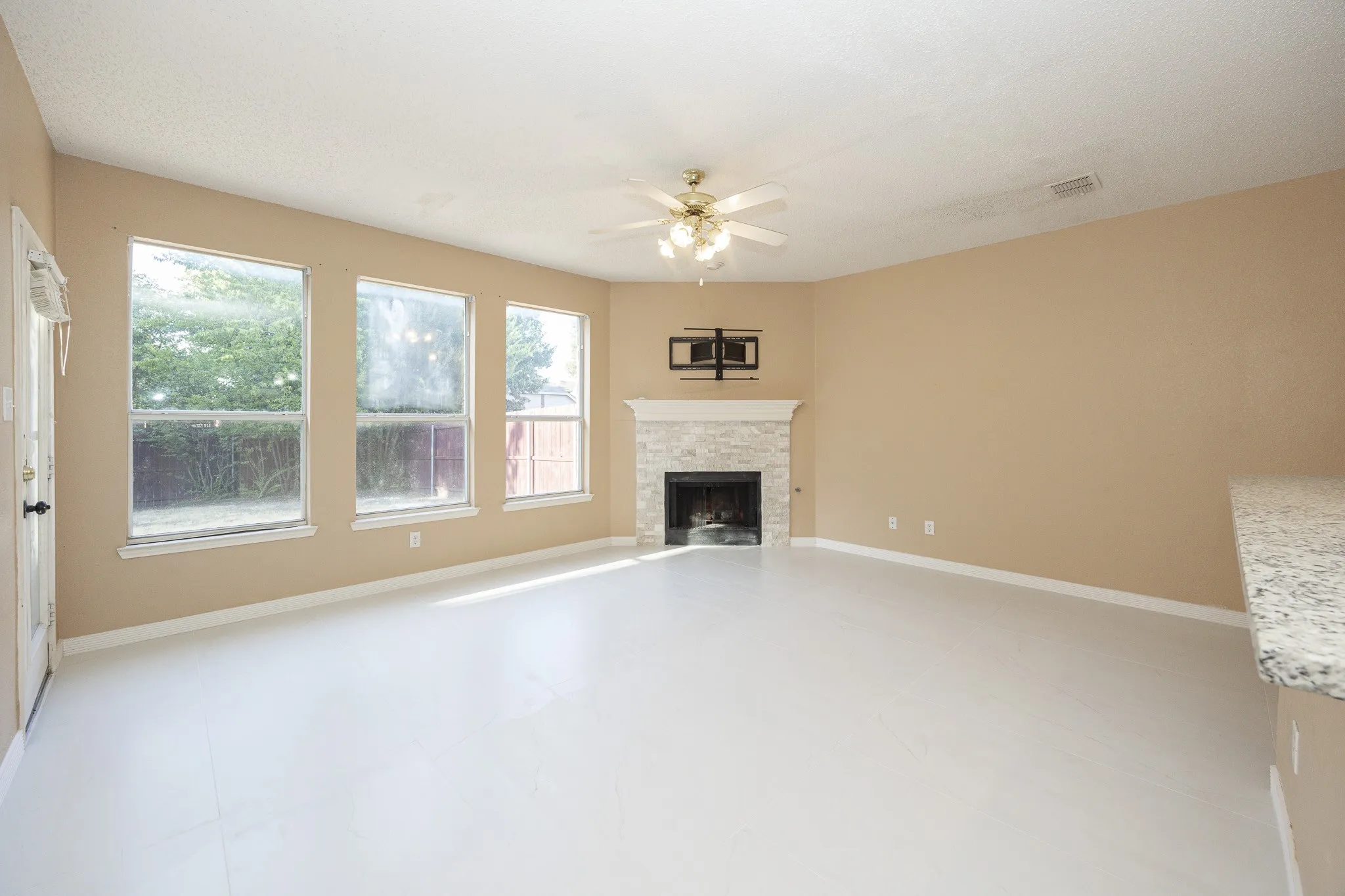 Spacious room with light-toned walls, multiple large windows, and a built-in fireplace featuring a stone surround and mantle