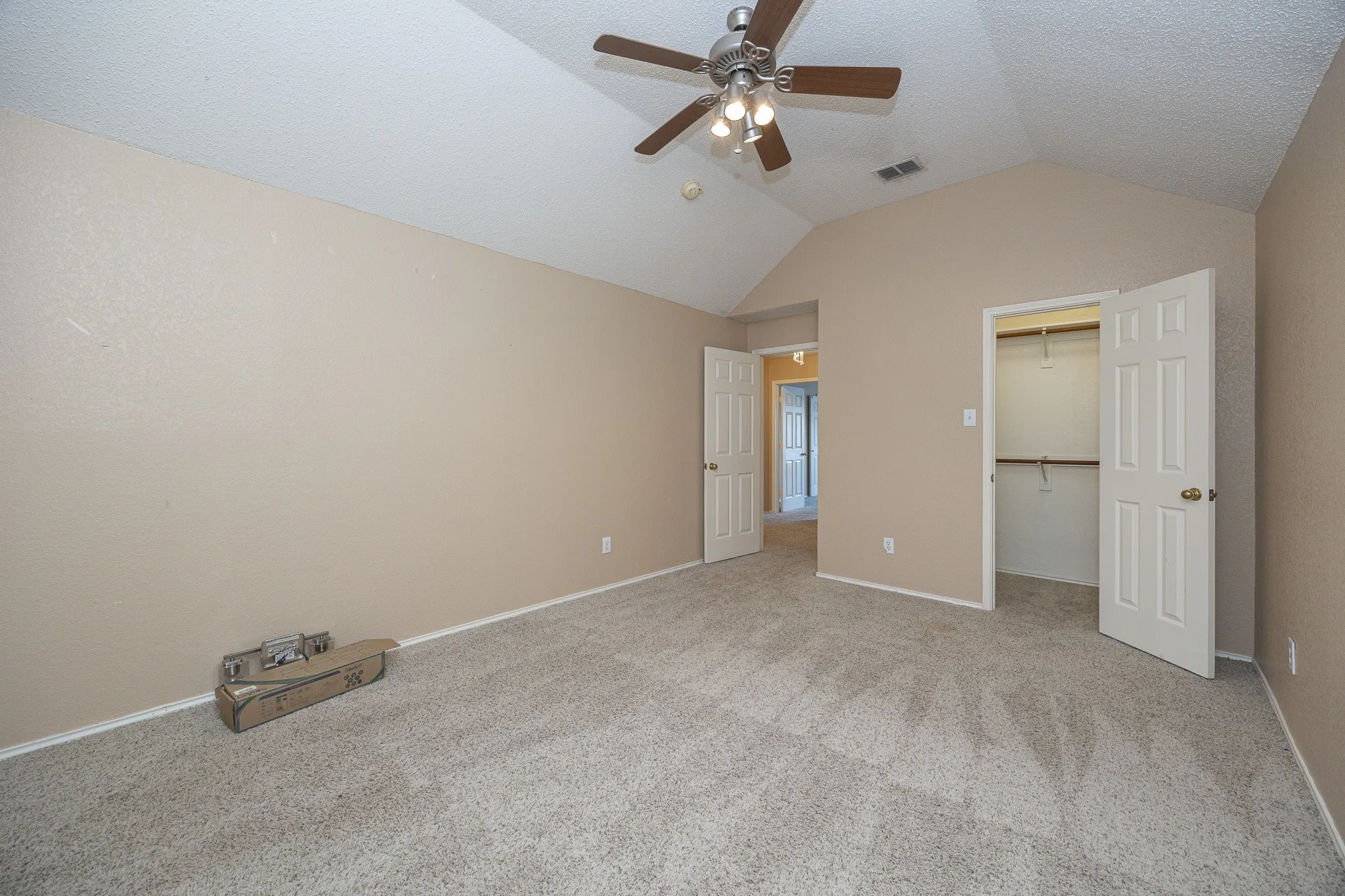 Vaulted ceiling, ceiling fan, neutral wall paint, carpet flooring, and a walk-in closet with shelving