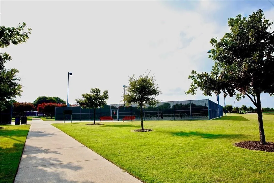 Expansive green space with a tennis court, concrete pathway, and mature trees