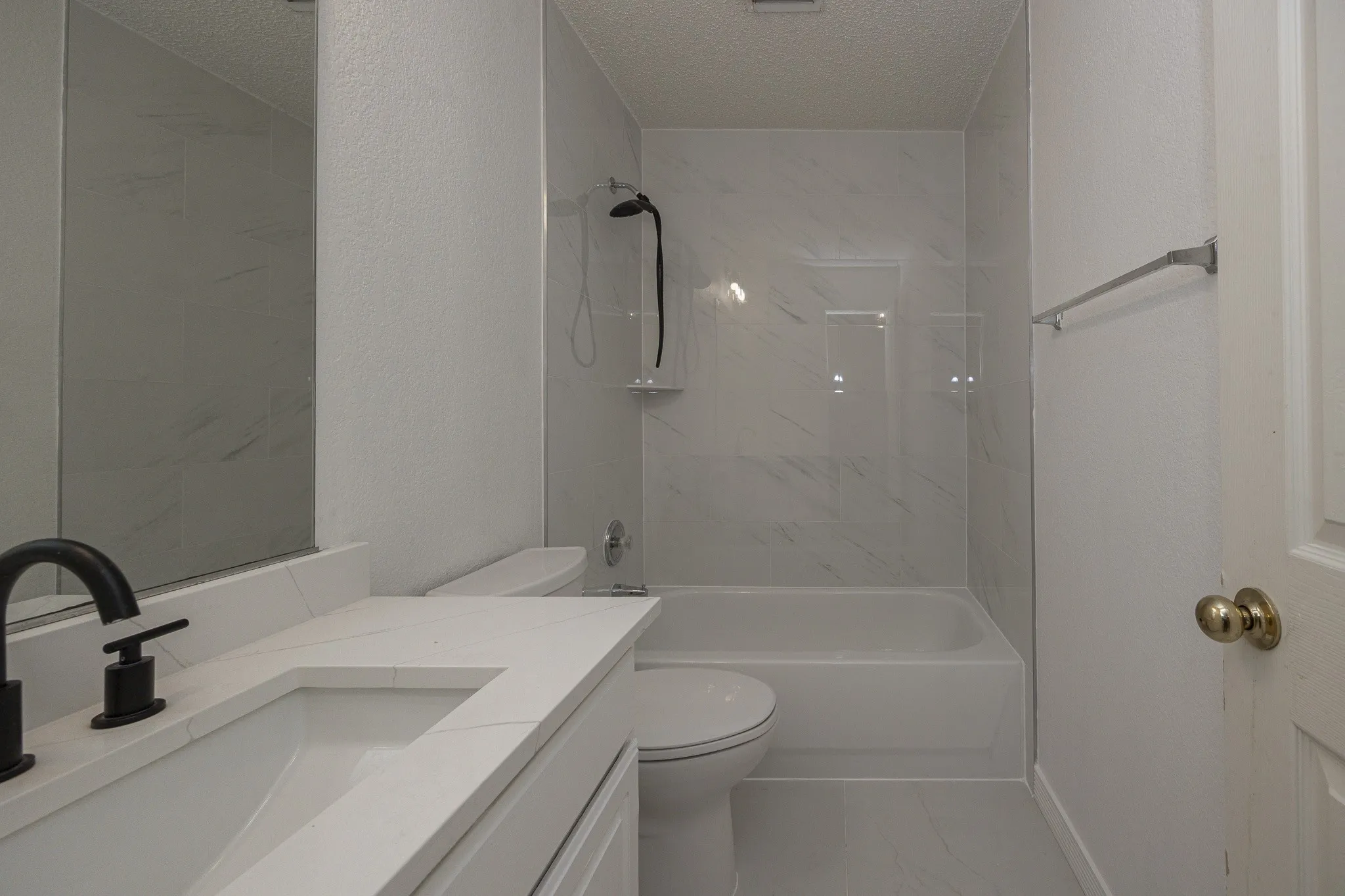 Bathroom featuring a white vanity with integrated sink, black fixtures, a mirrored wall, and a bathtub with a tiled surround
