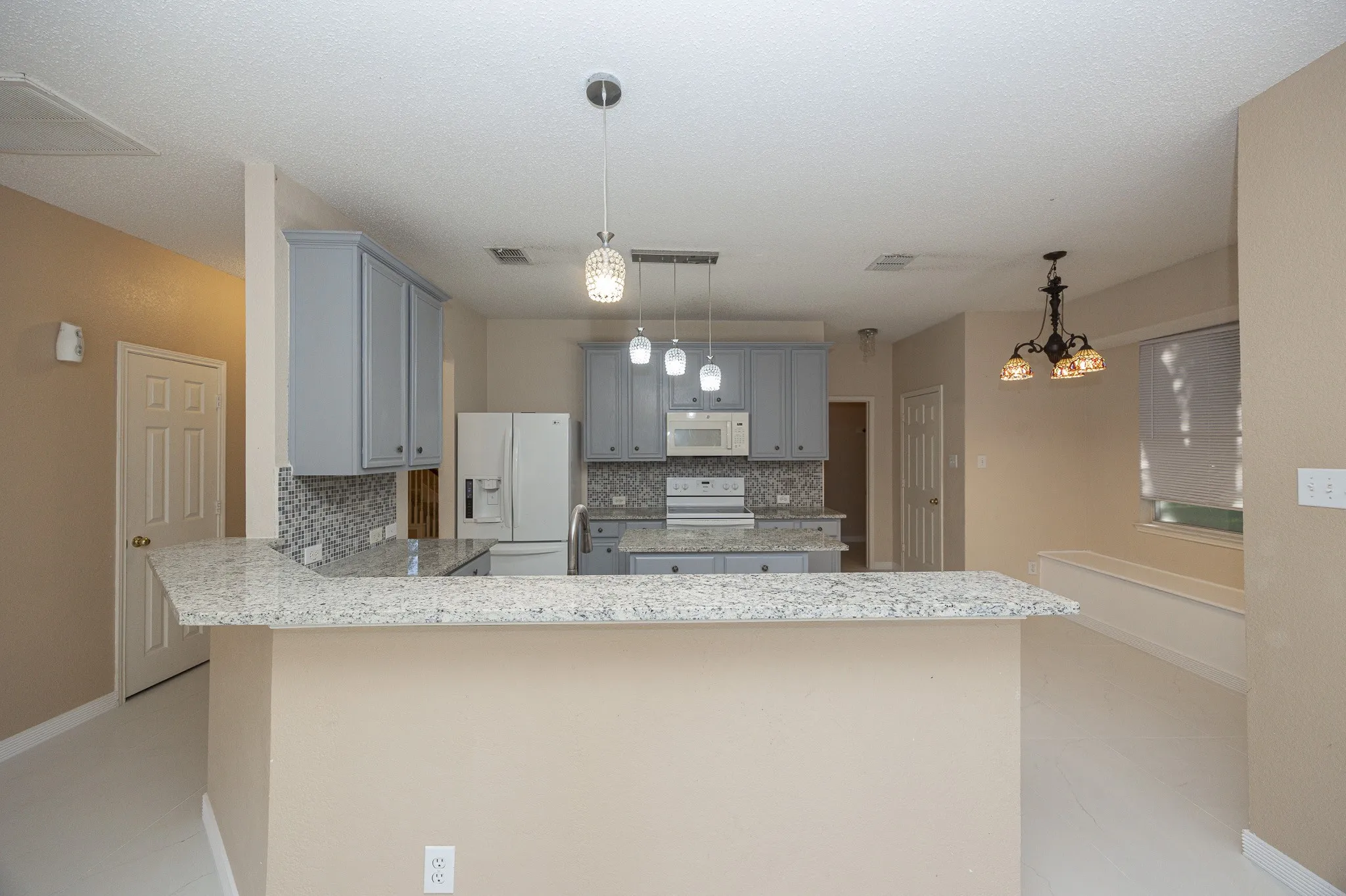 Granite countertops, gray cabinetry, mosaic tile backsplash, stainless steel appliances, and pendant lighting