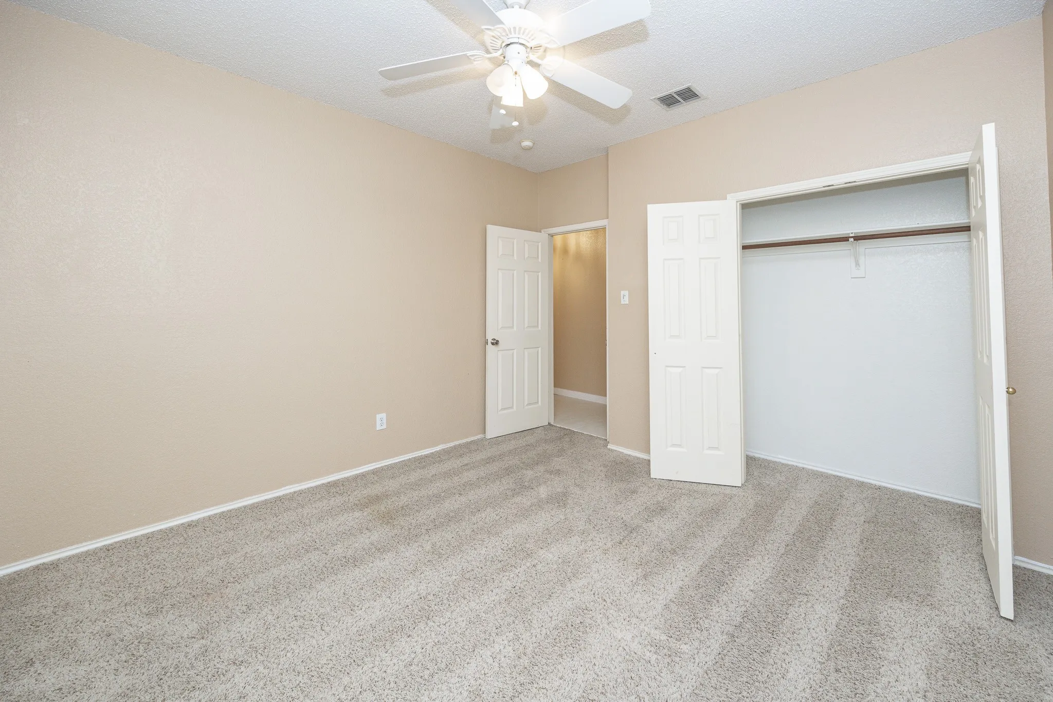 Neutral-toned walls, ceiling fan with integrated lighting, textured carpet flooring, and a built-in closet with bi-fold doors
