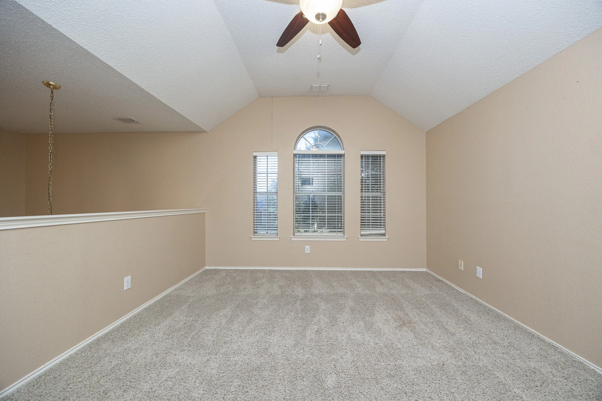 Vaulted ceiling, ceiling fan, carpet flooring, arched window, and architectural railing