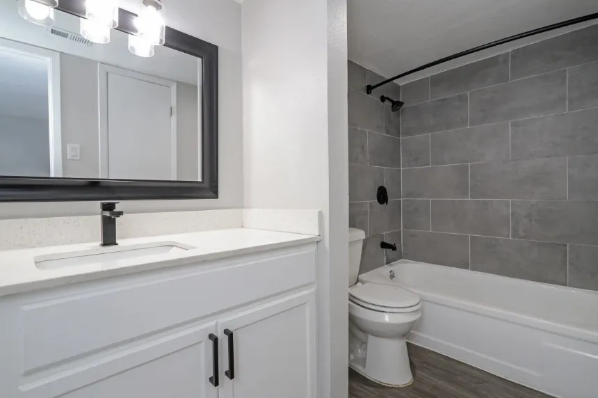 Modern bathroom featuring a floating vanity with white cabinetry, quartz countertop, and matte black hardware, paired with a framed mirror and contemporary lighting