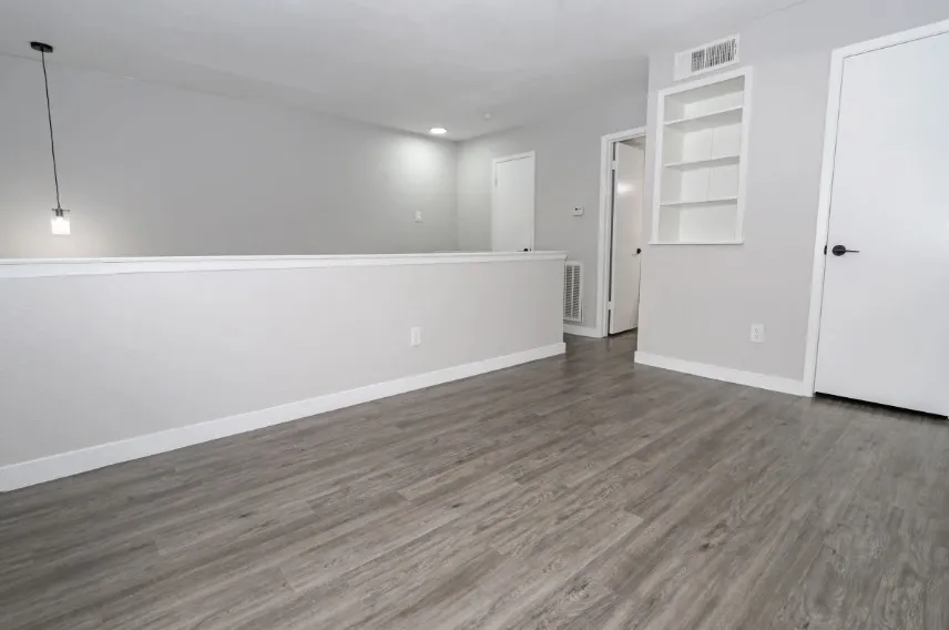 Spacious room featuring wood-finish flooring throughout, half-wall wainscoting with crisp white trim, recessed lighting, and multiple closet and door entries