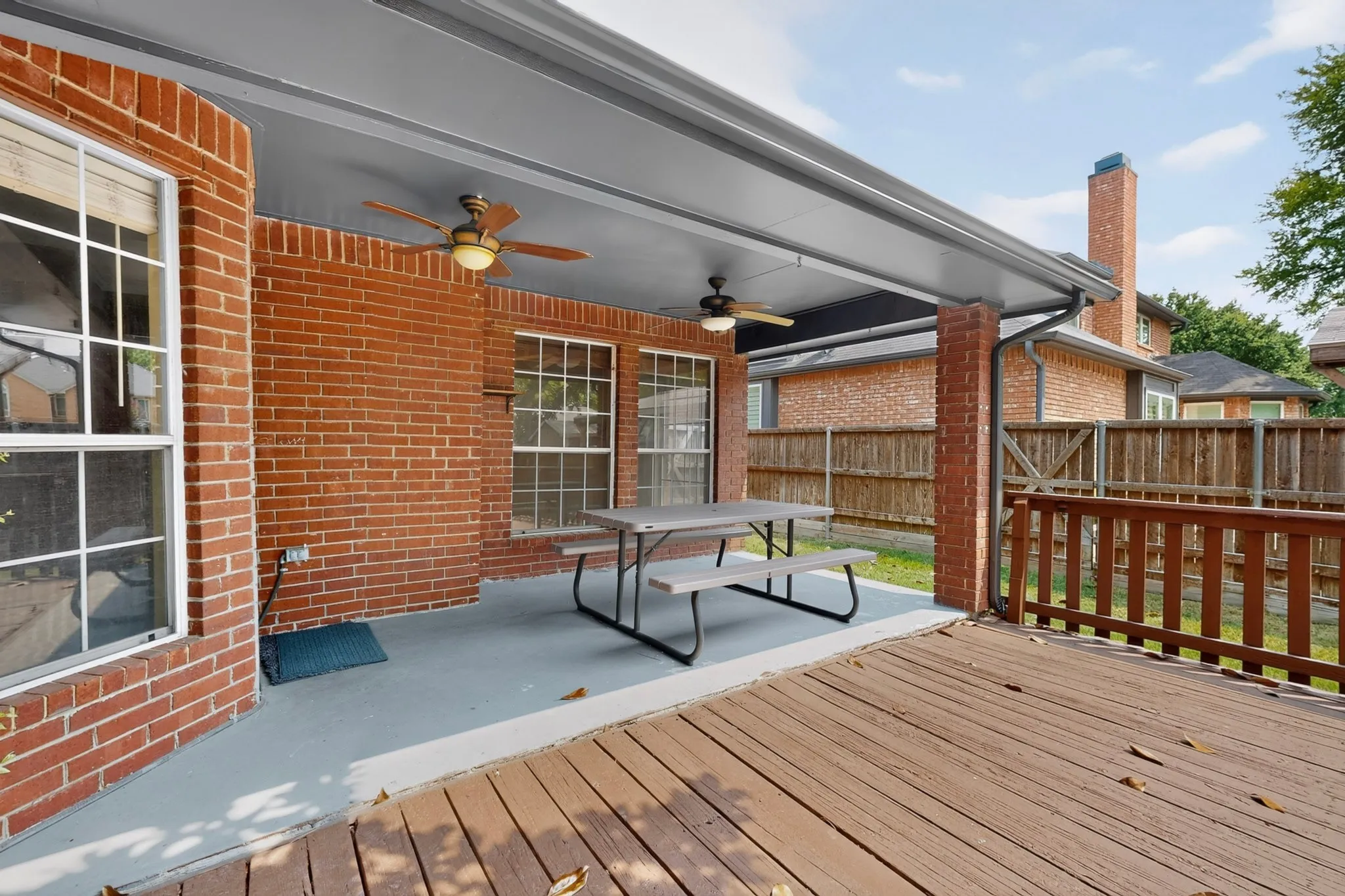 Covered patio with brick columns and ceiling fans, complemented by an expansive wood-finish deck and privacy fencing