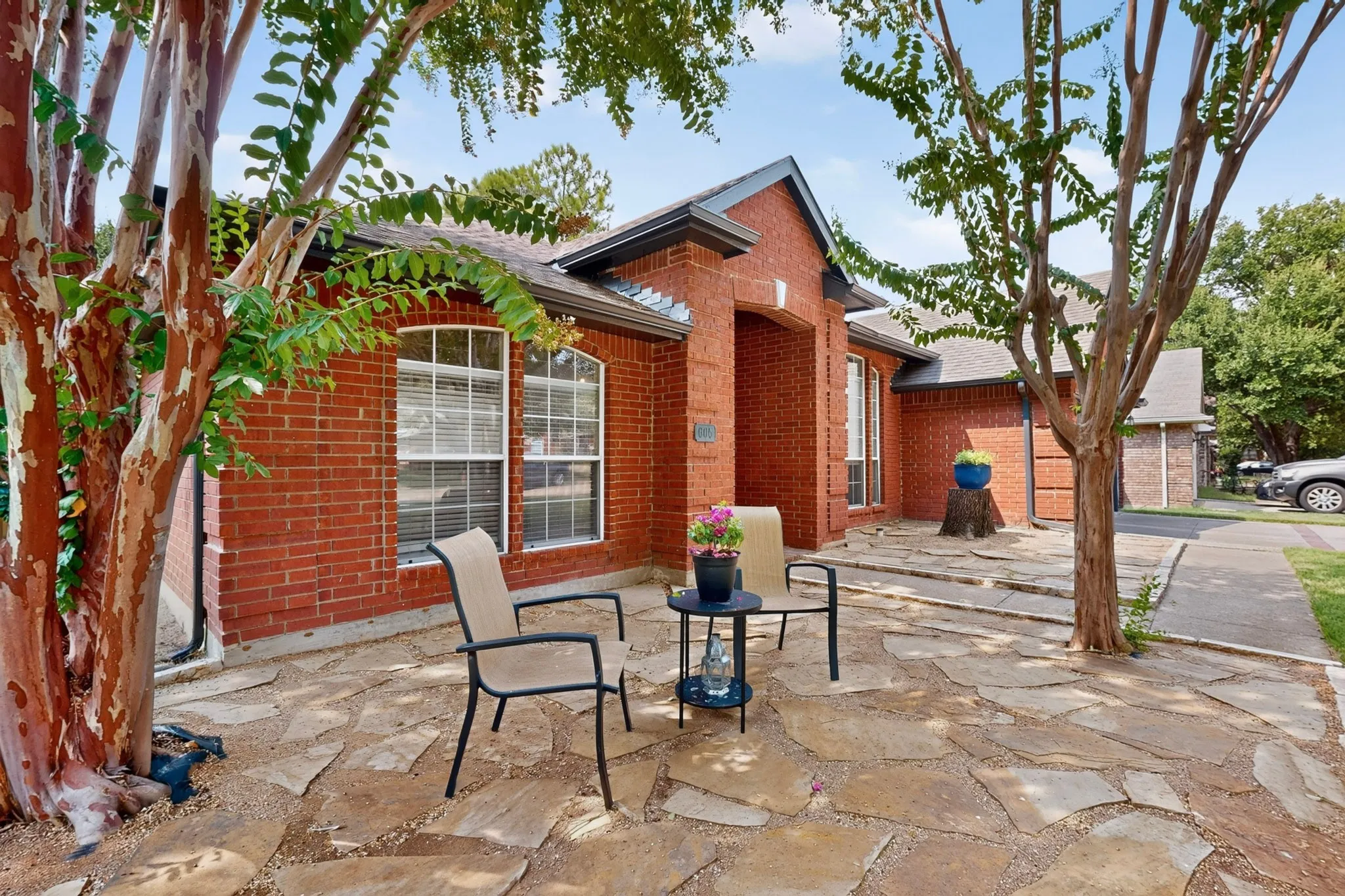 Red brick exterior with arched window, flagstone patio, and mature trees