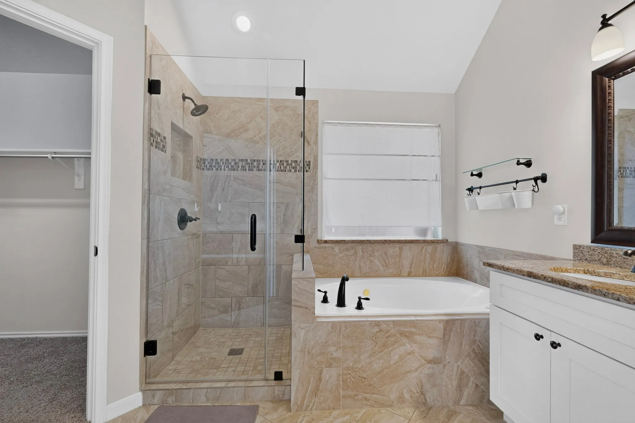 Glass-enclosed shower with stone-look tile, built-in shower niche, and dark-finish fixtures