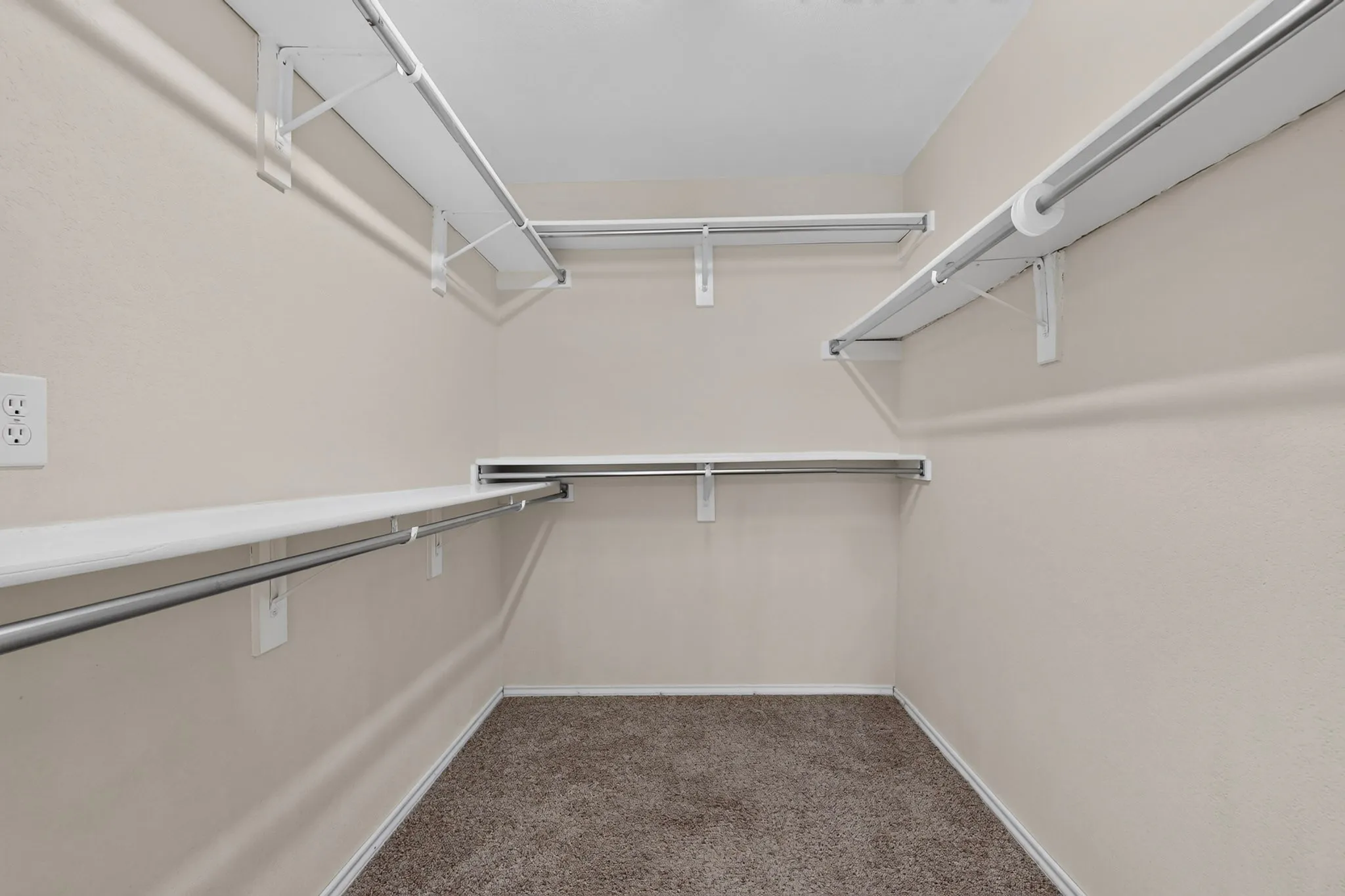 Primary suite walk-in closet featuring white wire shelving, chrome hanging rods, and carpet flooring