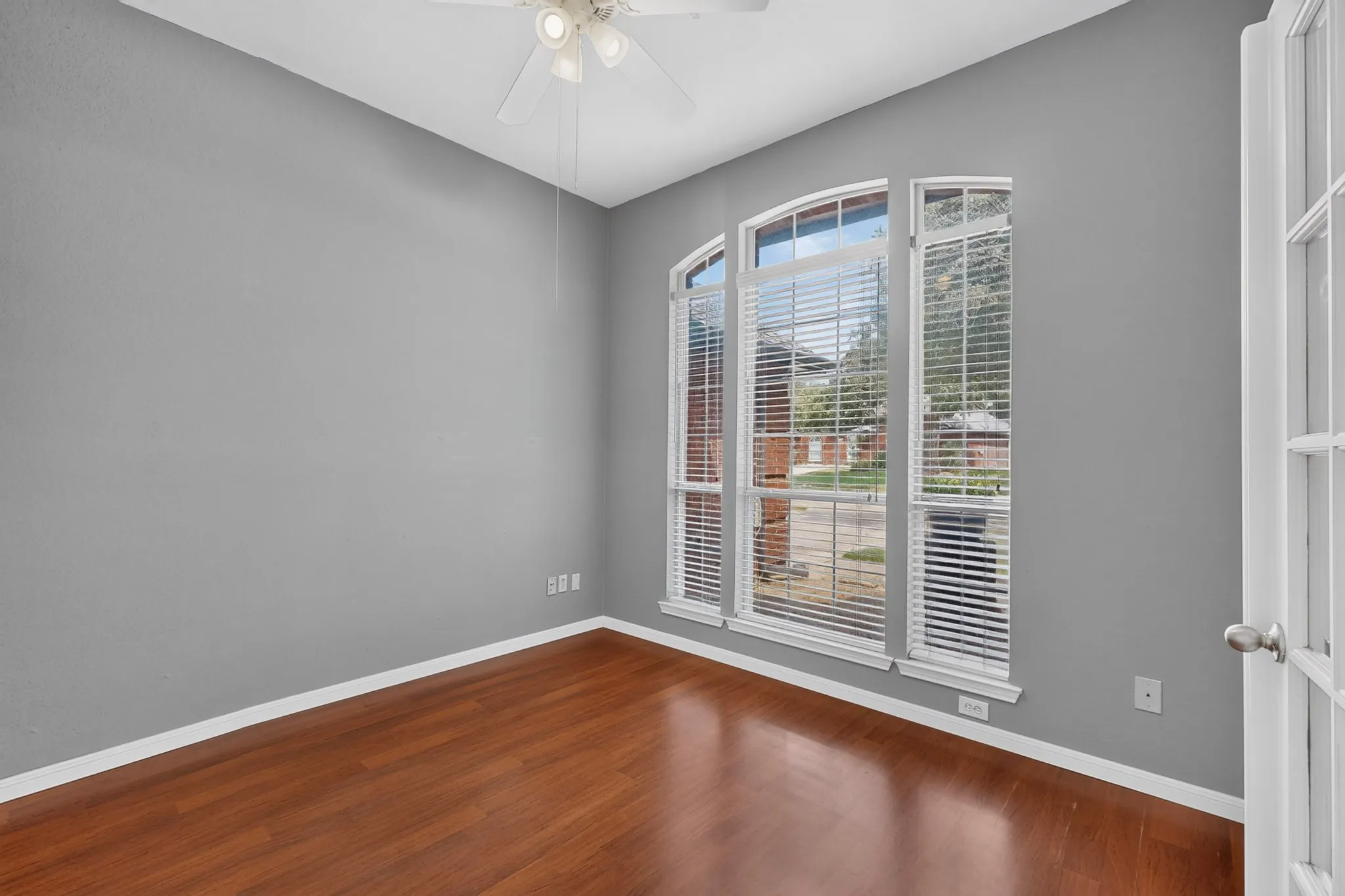 Home office with hardwood-style flooring, arched windows, ceiling fan, and French doors