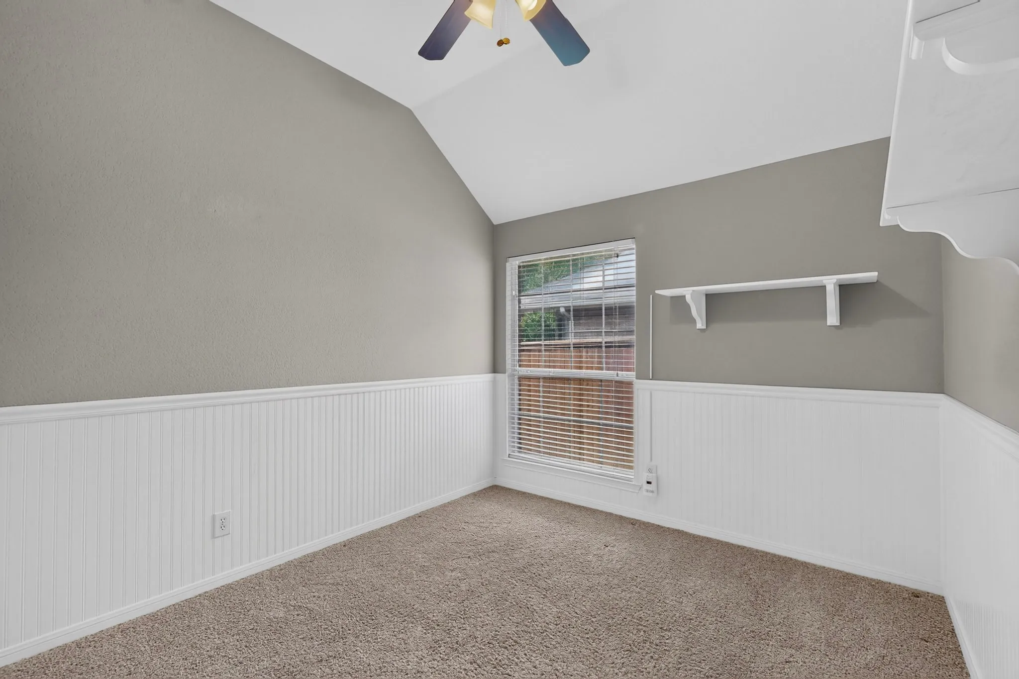 Vaulted ceiling, ceiling fan, window with blinds, beadboard wainscoting, and wall shelving