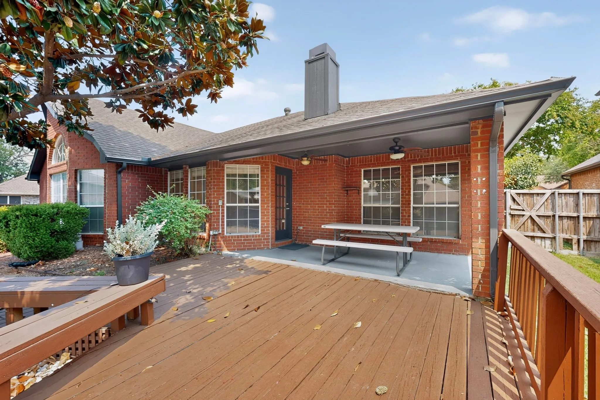 Expansive multi-level wood deck, brick exterior, covered patio, outdoor ceiling fan, and mature landscaping