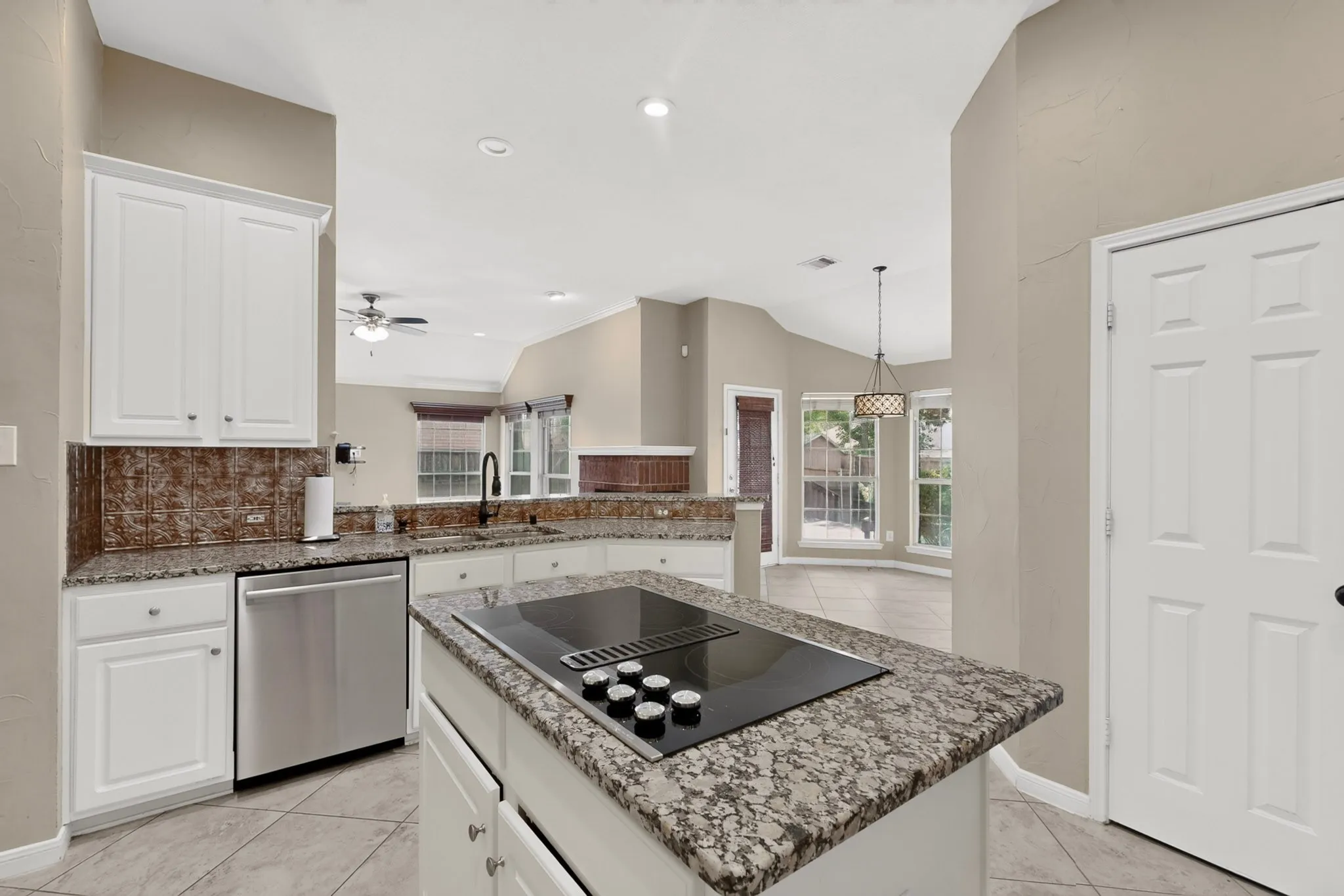 Kitchen with white cabinetry, granite countertops, tile flooring, a stainless steel dishwasher, and an island cooktop