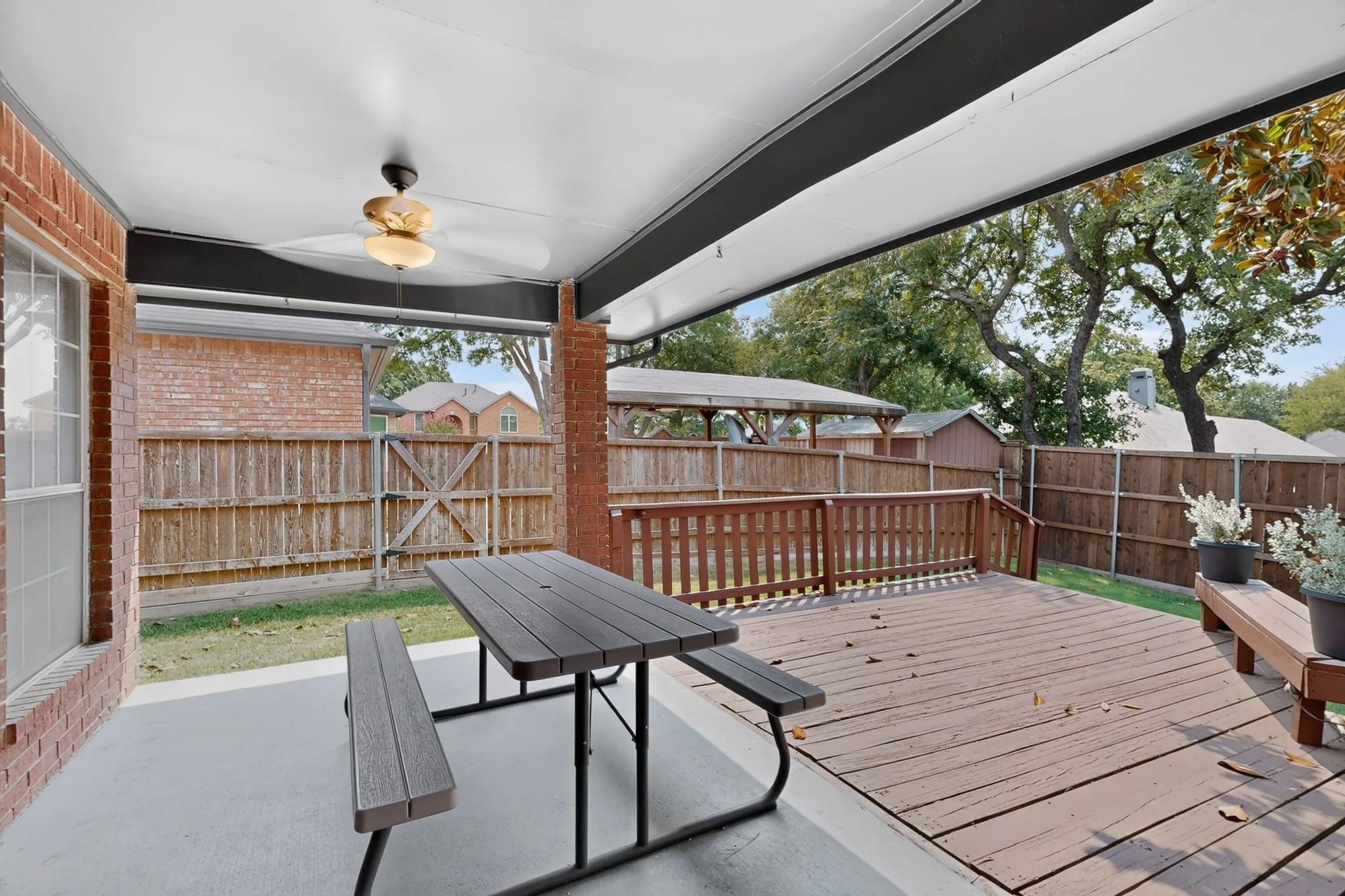Covered patio with a ceiling fan, brick exterior, and wood-finish deck with a railing