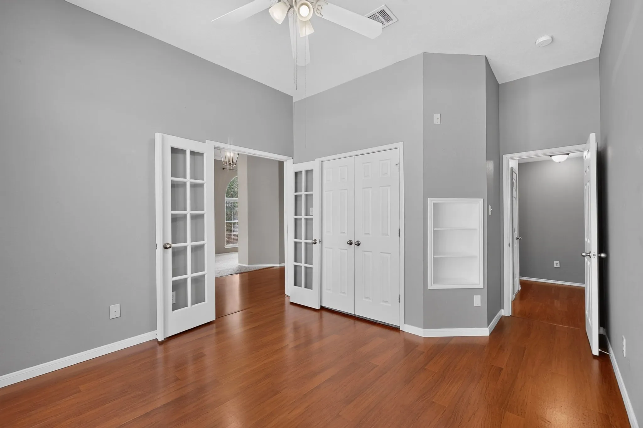 Home office with hardwood-style flooring, arched windows, ceiling fan, and French doors