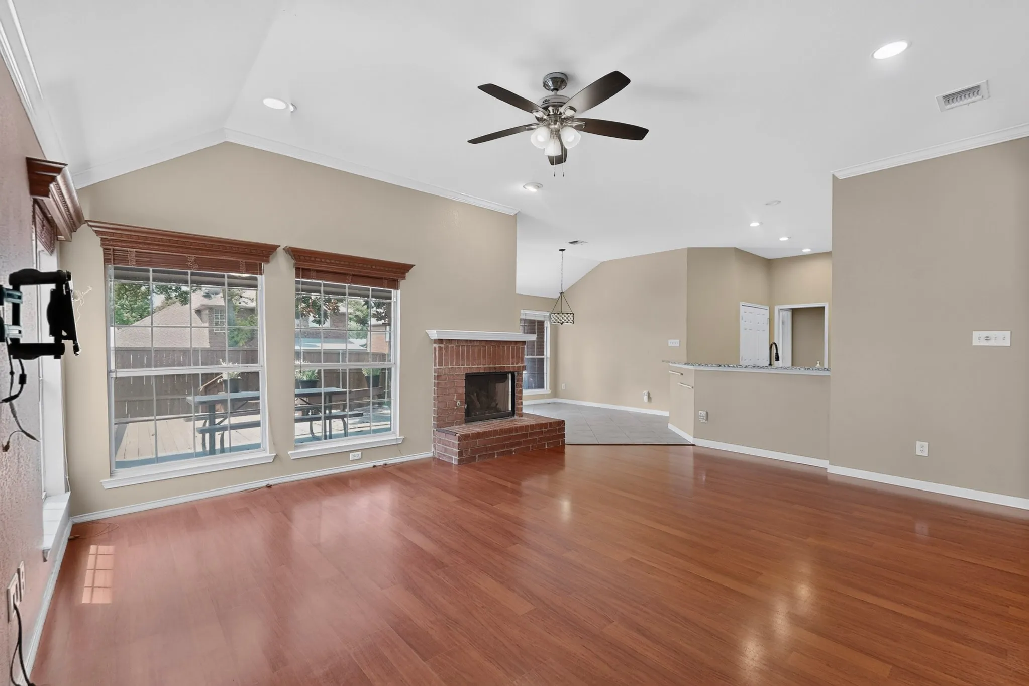 Vaulted ceiling with recessed lighting, wood-finish flooring, brick fireplace, ceiling fan, and large windows with blinds