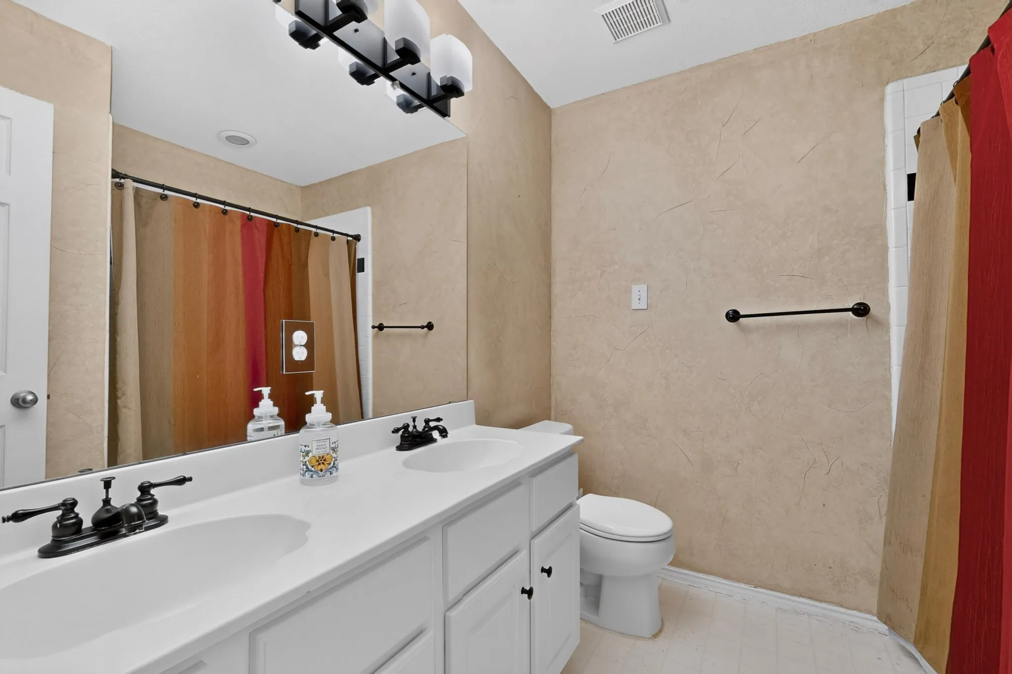 Dual vanity with white cabinetry, matte black fixtures, and an expansive mirror
