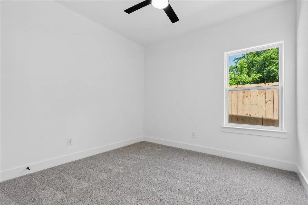 White interior walls with gray carpet flooring and a ceiling fan