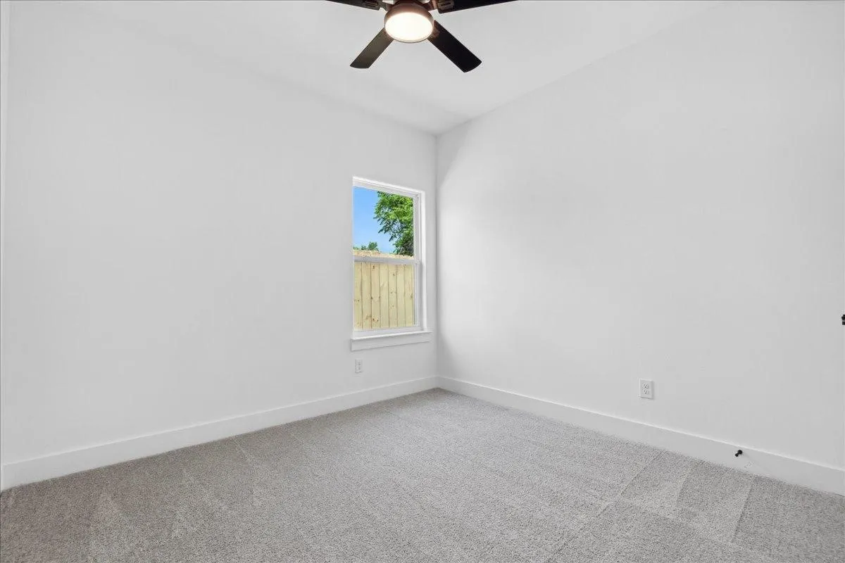 Carpeted room featuring a ceiling fan, white walls, and a window with natural light