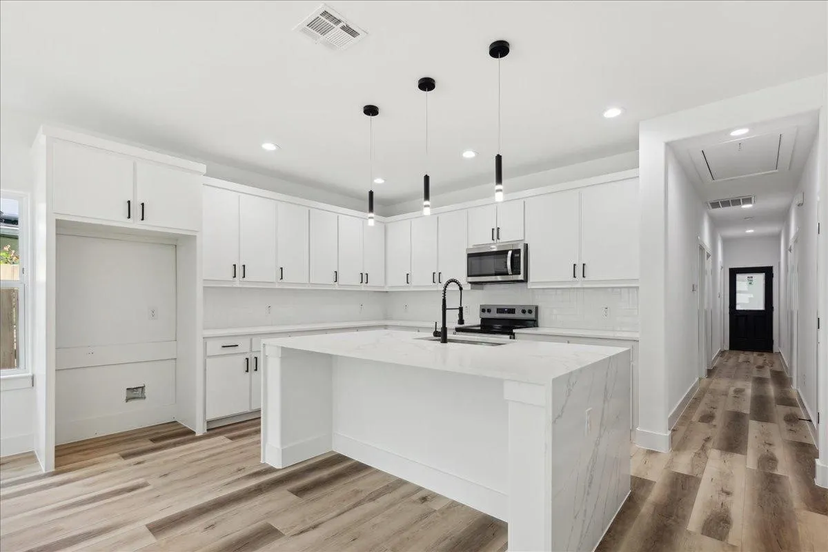 Modern kitchen featuring white cabinetry, a large center island with a stone countertop, stainless steel appliances, and wood-finish flooring