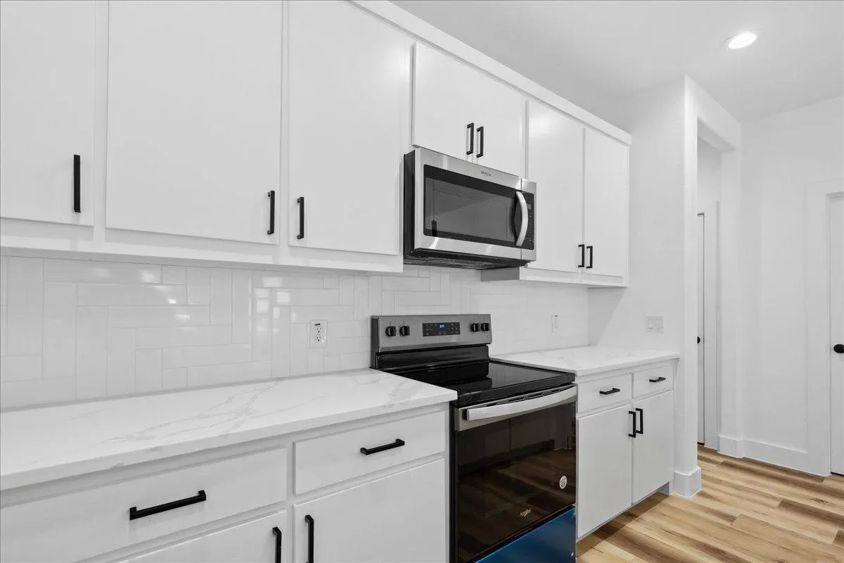 Modern kitchen featuring white shaker-style cabinetry with matte black hardware, stainless steel appliances including a slide-in range and overhead microwave, white subway tile backsplash, and quartz countertops