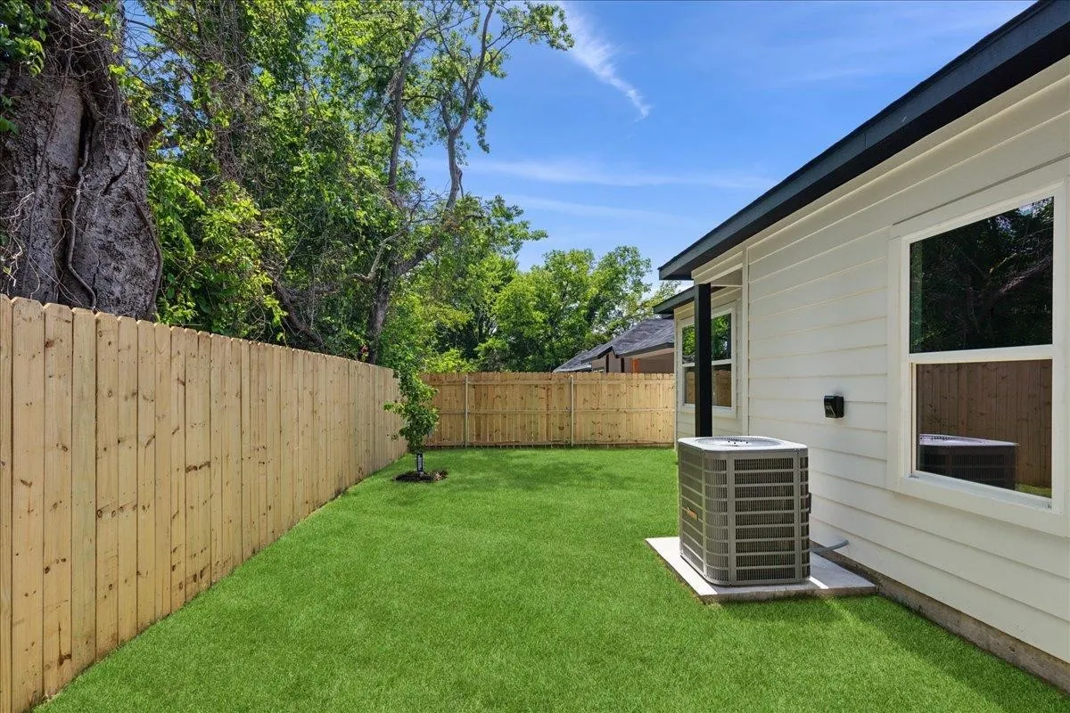 Expansive backyard featuring a manicured lawn, full privacy fencing, and mature trees