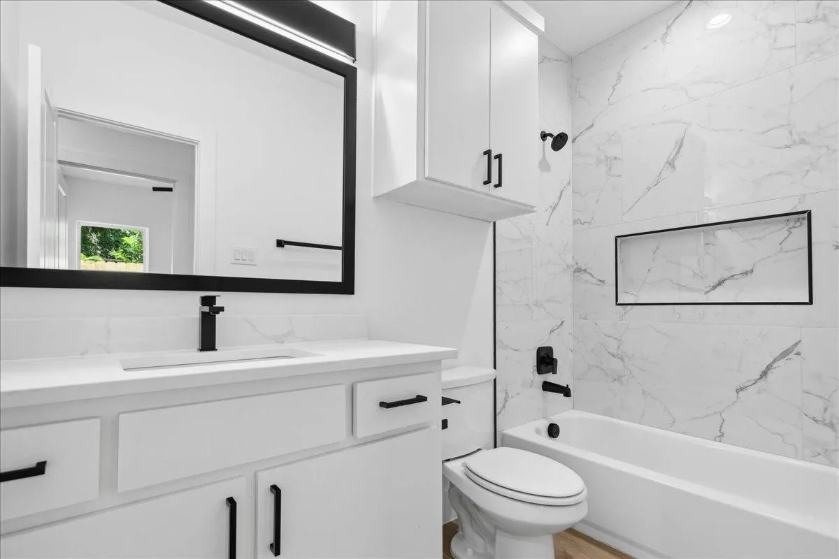 White vanity with integrated sink, black hardware, and an illuminated rectangular mirror