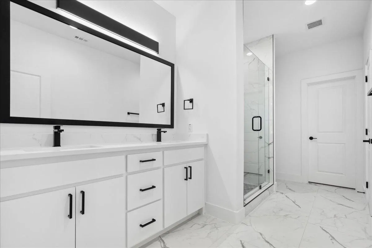 Dual vanity with matte black faucets, white cabinetry, and a full-width mirror
