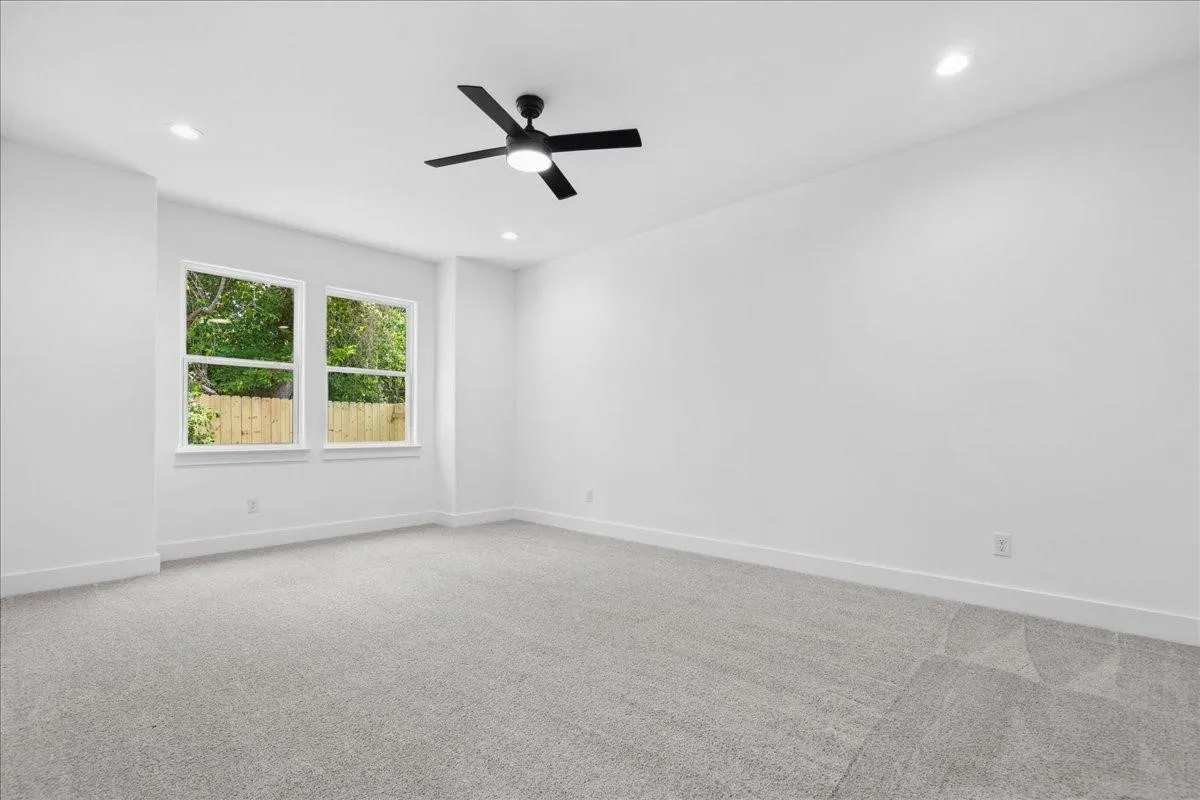 Bright, light-filled bedroom with recessed ceiling lighting, modern ceiling fan with four blades, and dual windows framed in white trim offering natural light