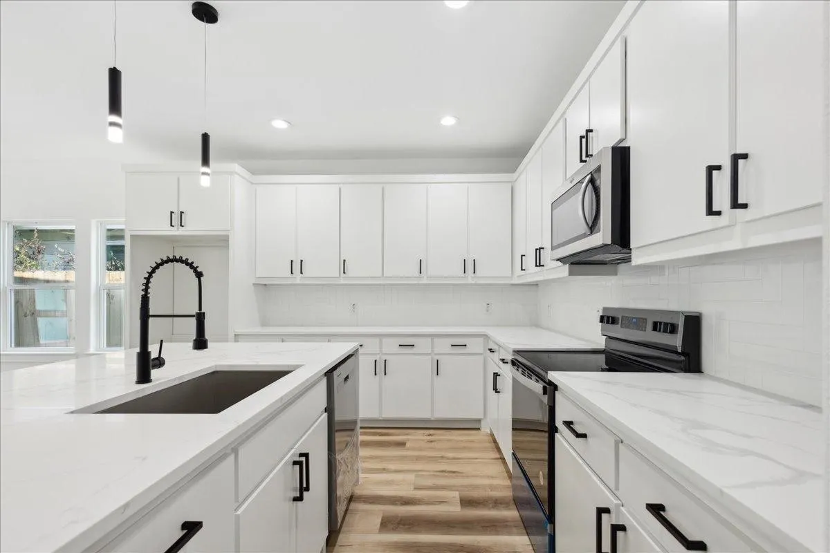 Modern kitchen featuring white cabinetry, stainless steel appliances, light-toned countertops, wood-finish flooring, and a black-finish faucet